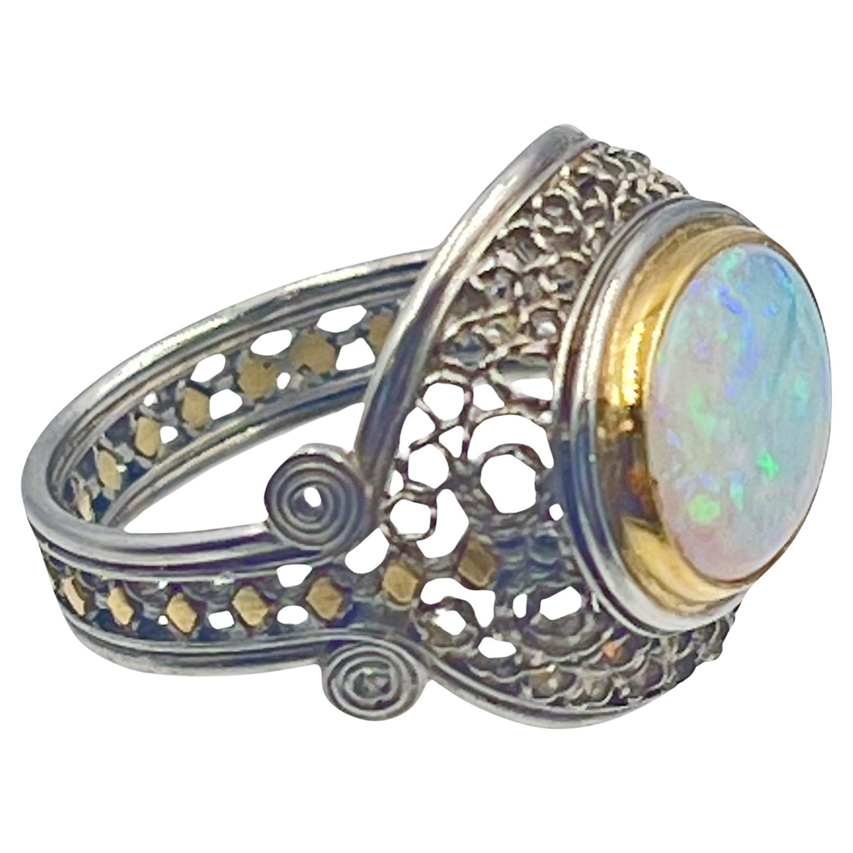 Handmade opal ring in platinum and 18k yellow gold by New York jewelry designer Judy Geib.  Central cabochon cut 12 x 9mm pinfire opal, horizontally set in an 18 karat yellow gold bezel. The opal has a vibrant green, blue, and orange play of color. 