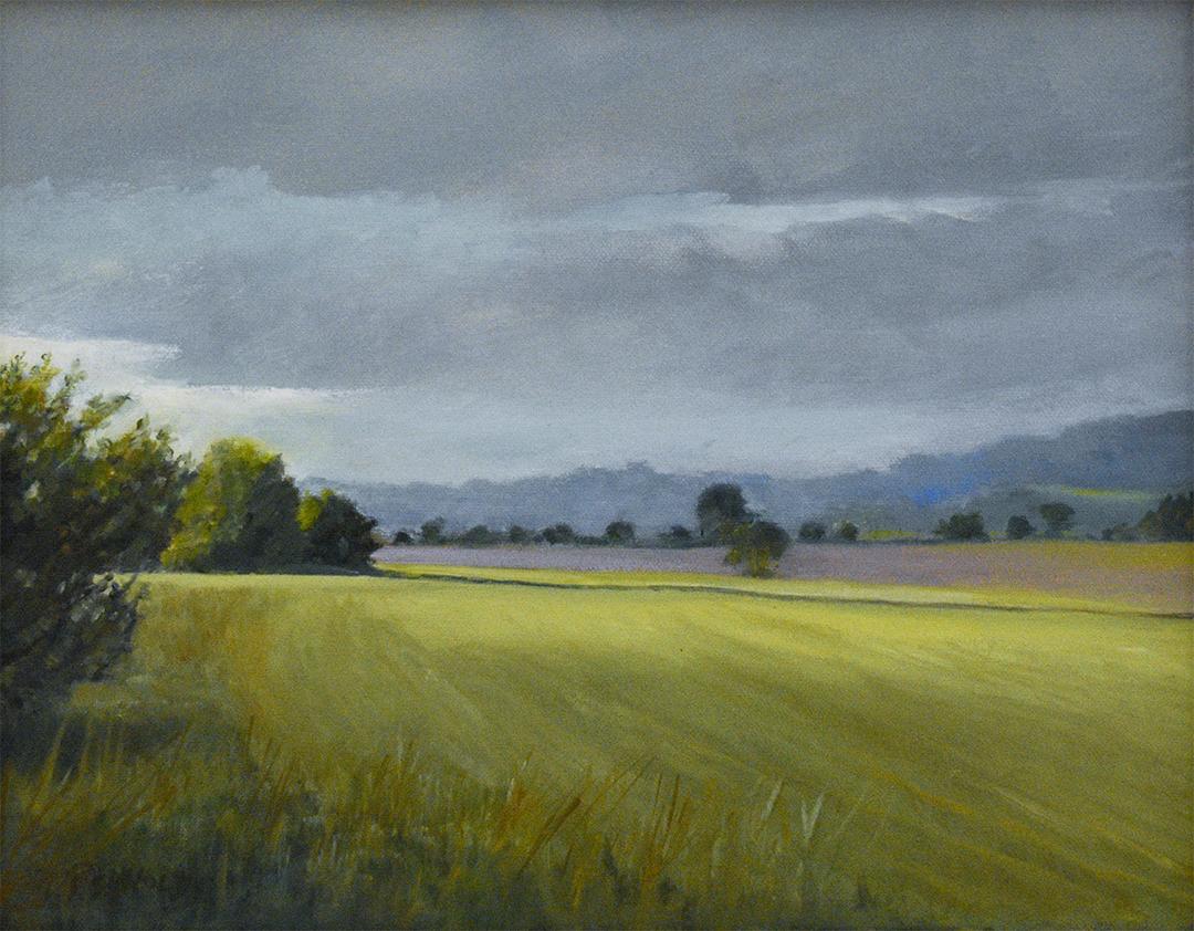 En plein air landscape oil painting on canvas of a lush sunlit green country field and blue mountains under a blue and grey clouded sky 
