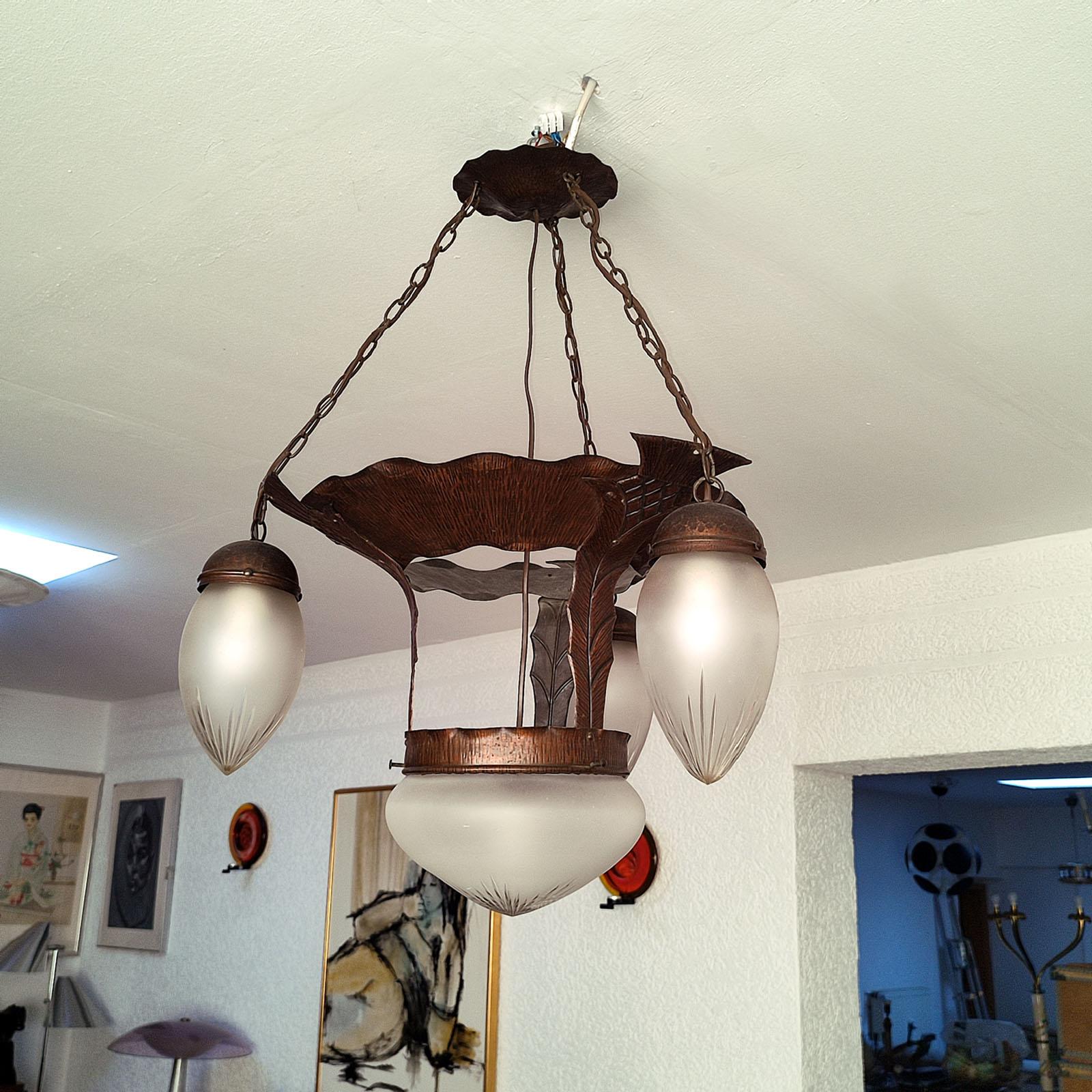 Belle suspension suédoise Jugendstil des années 1910-1920. Le corps est en cuivre, entièrement martelé. Trois lumières sont encastrées sur le pourtour et une centrale avec un diffuseur en verre satiné taillé. Quatre douilles E27 en céramique