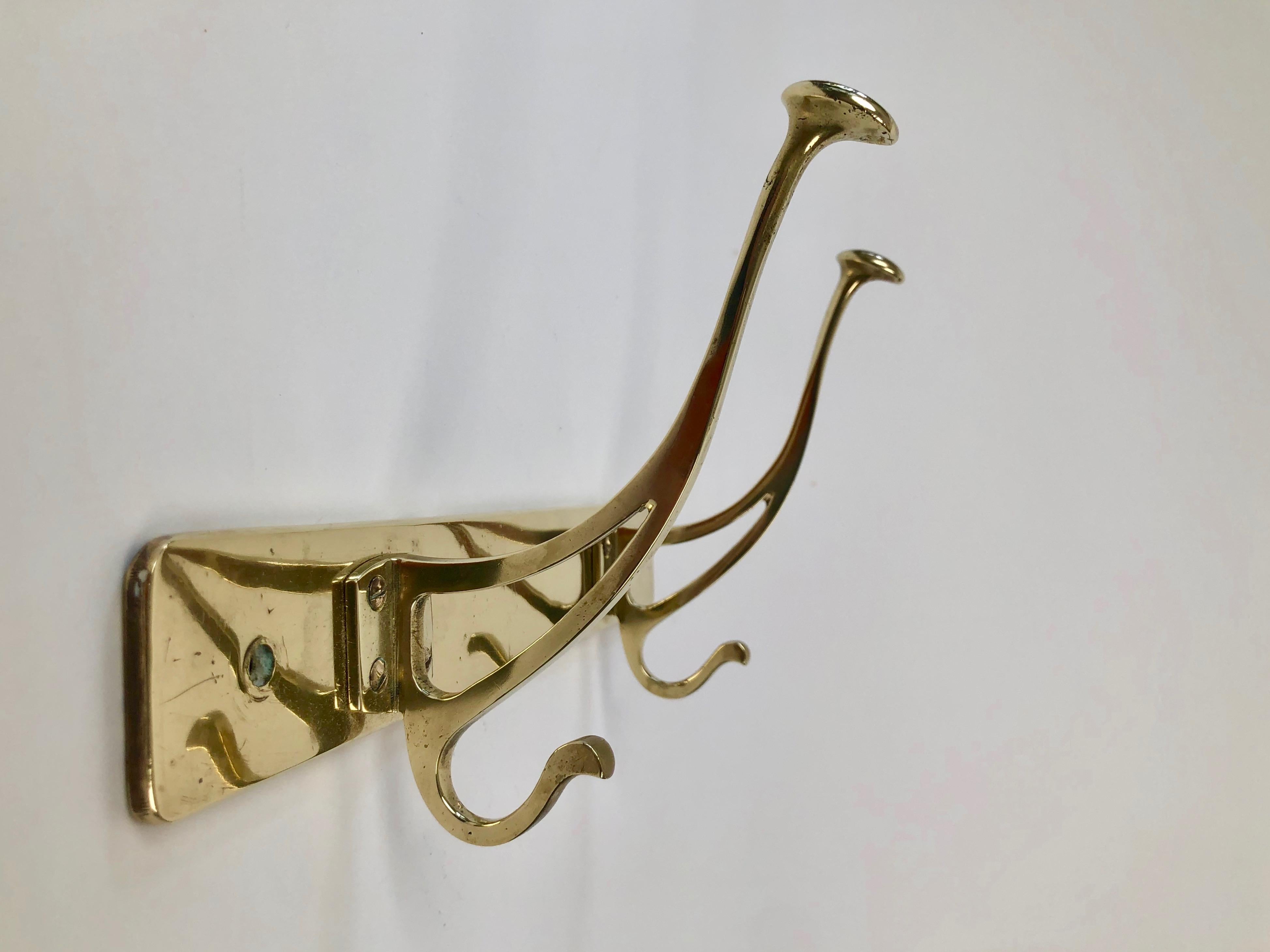 A useful, simple, elegant coat rack from Jugendstil period produced in Austria. 
Composed of two solid brass coat hooks  attached to a base plate made up from
brass sheet metal, put under pressure and formed around an iron base. 
This process is