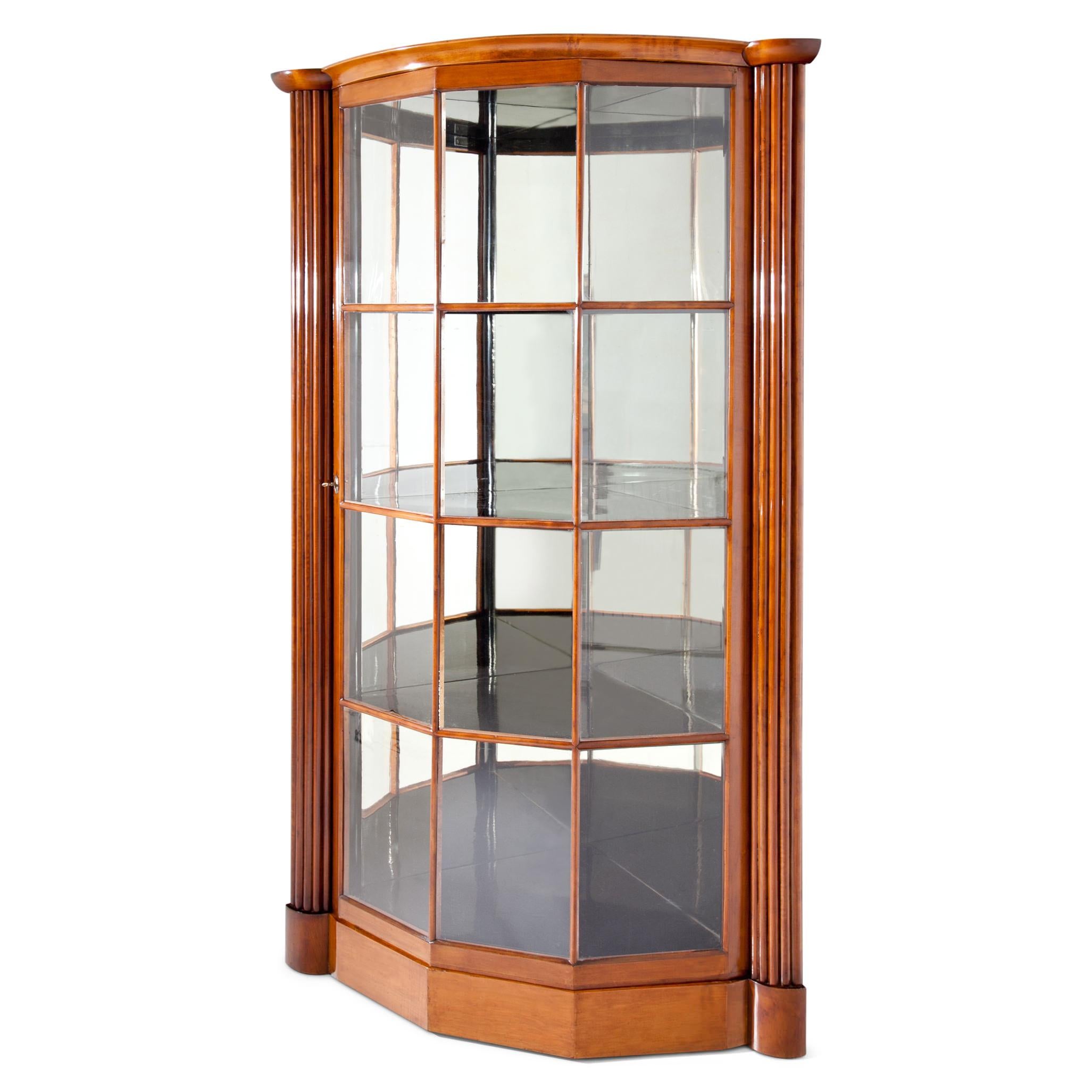 Corner display case with fluted pillars on the corners and a glazed door with wooden strutting. The inner walls are mirrored. Side length: 73 cm.