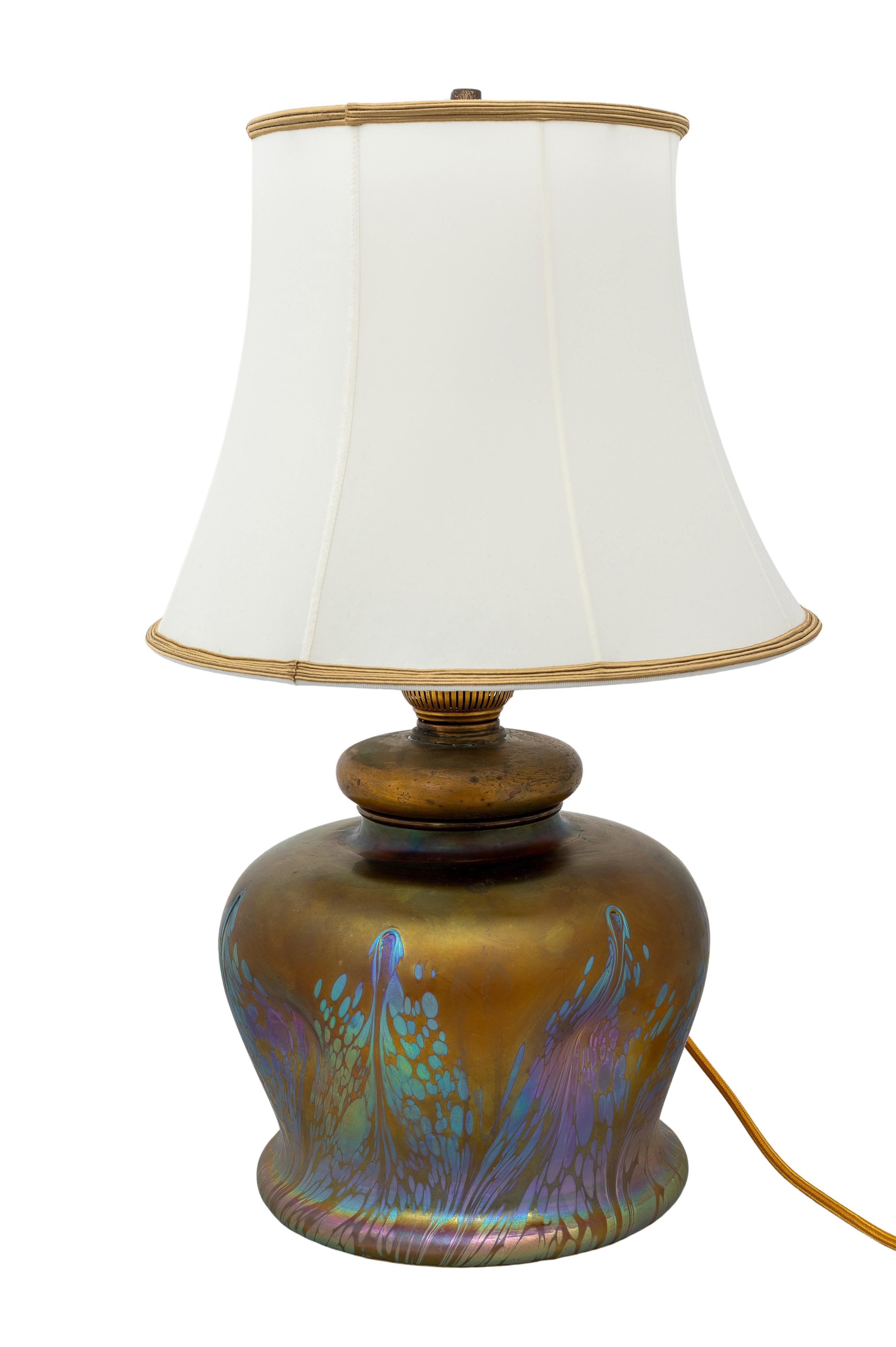 The body of the lamp is manufactured by Johann Loetz Witwe for E. Bakalowits Söhne, ca. 1902. The glass is mould-blown and freeform, reduced and iridescent with Medici PG 2/484 decoration.  The lampshade is new and handmade in Vienna with