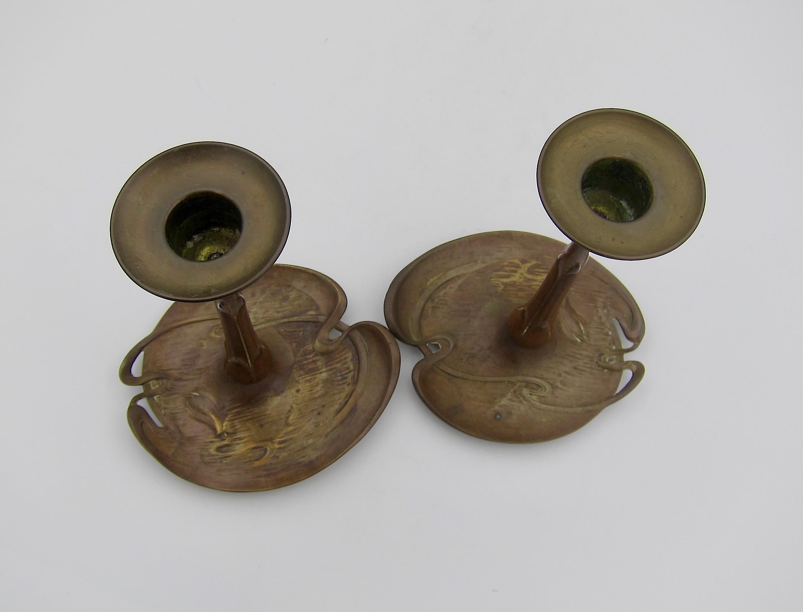 A pair of European art metal candle holders made in Austria or Germany at the turn of the 20th century. The antique base metal of bronze or brass has a rich golden brown patina with hints of red in the finish. Each candlestick was cast to resemble a