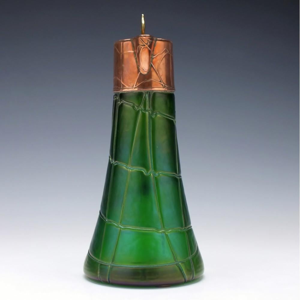 A rare Jugenstil/Art Nouveau Pallme-König glass spider trailing claret jug.

Iridescent green

Copper plated cap. The copper has matching relief trailing – an unusual feature. The hinge is in perfect functional condition. Angled handle with