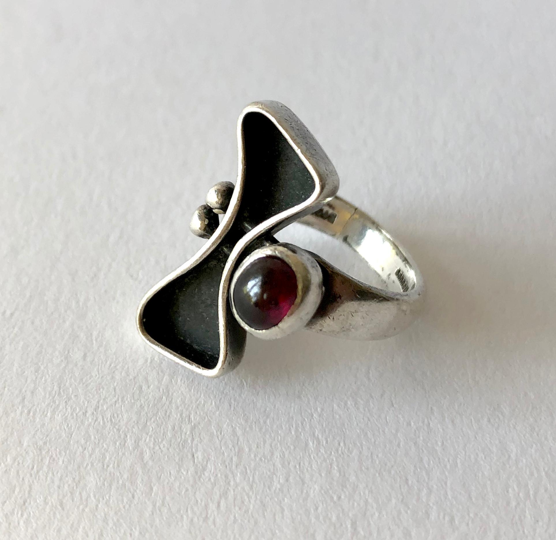 Sterling silver with garnet cabochon modernist ring, created by painter, sculptor and jeweler Jules Brenner of New York City.  Ring is a finger size 5.5 and is signed Jules Brenner on the shank.  In very good vintage condition showing signs of wear