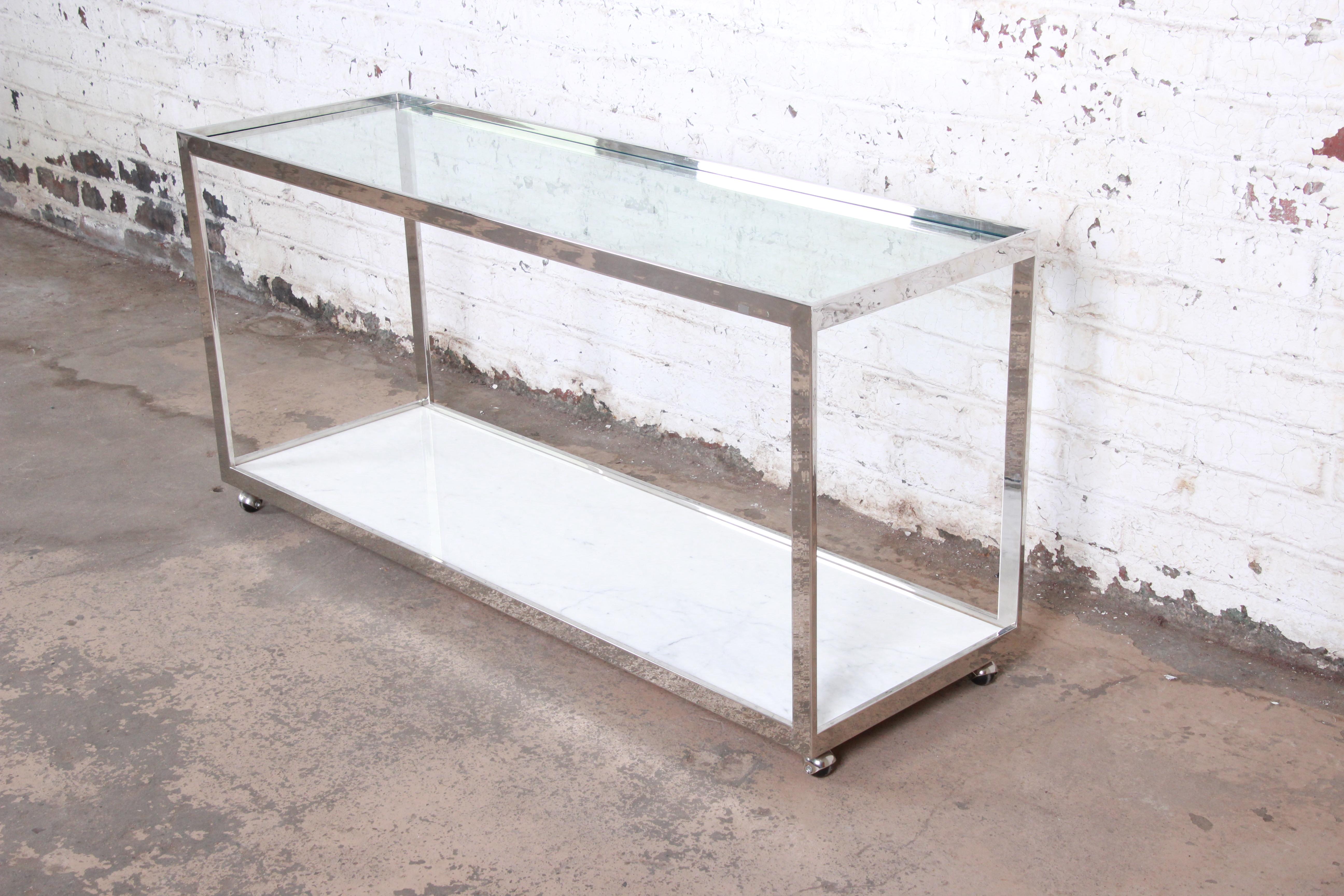 A gorgeous Mid-Century Modern console table designed by Jules Heumann for Metropolitan Furniture, circa 1950s. The table features a sleek polished chrome frame, with a glass top and stunning Carrara marble base. The console is on original casters