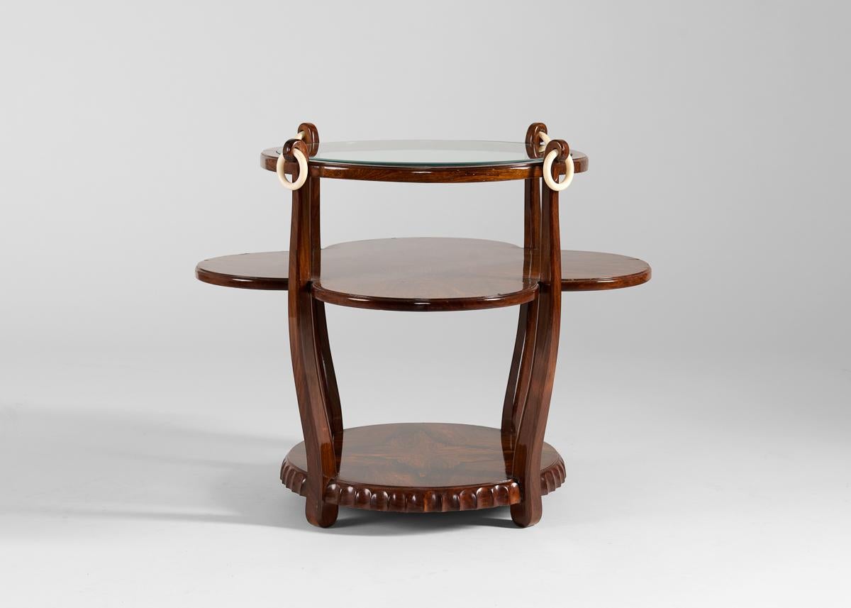 This charming tea table, designed by one of the period's greatest furniture designers, is the very consummation of French Art Deco elegance. The table's top—glass set in a circular top, dotted with bone rings—rests atop two broad levels of