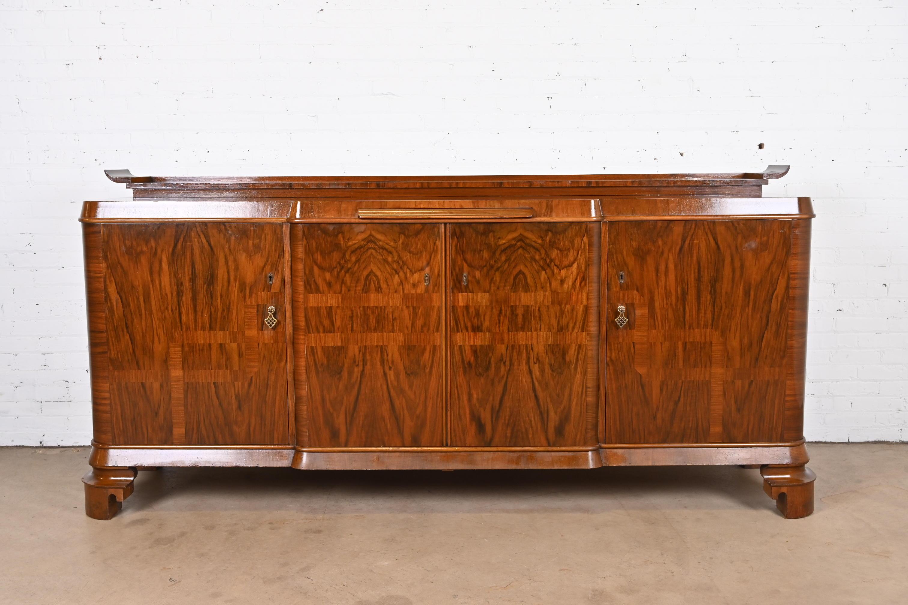 An exceptional monumental French Art Deco sideboard, credenza, or bar cabinet

In the manner of Jules Leleu

France, Circa 1930s

Stunning book-matched burled walnut with inlaid design, inset marble pull-out tray, and brass hardware. Key