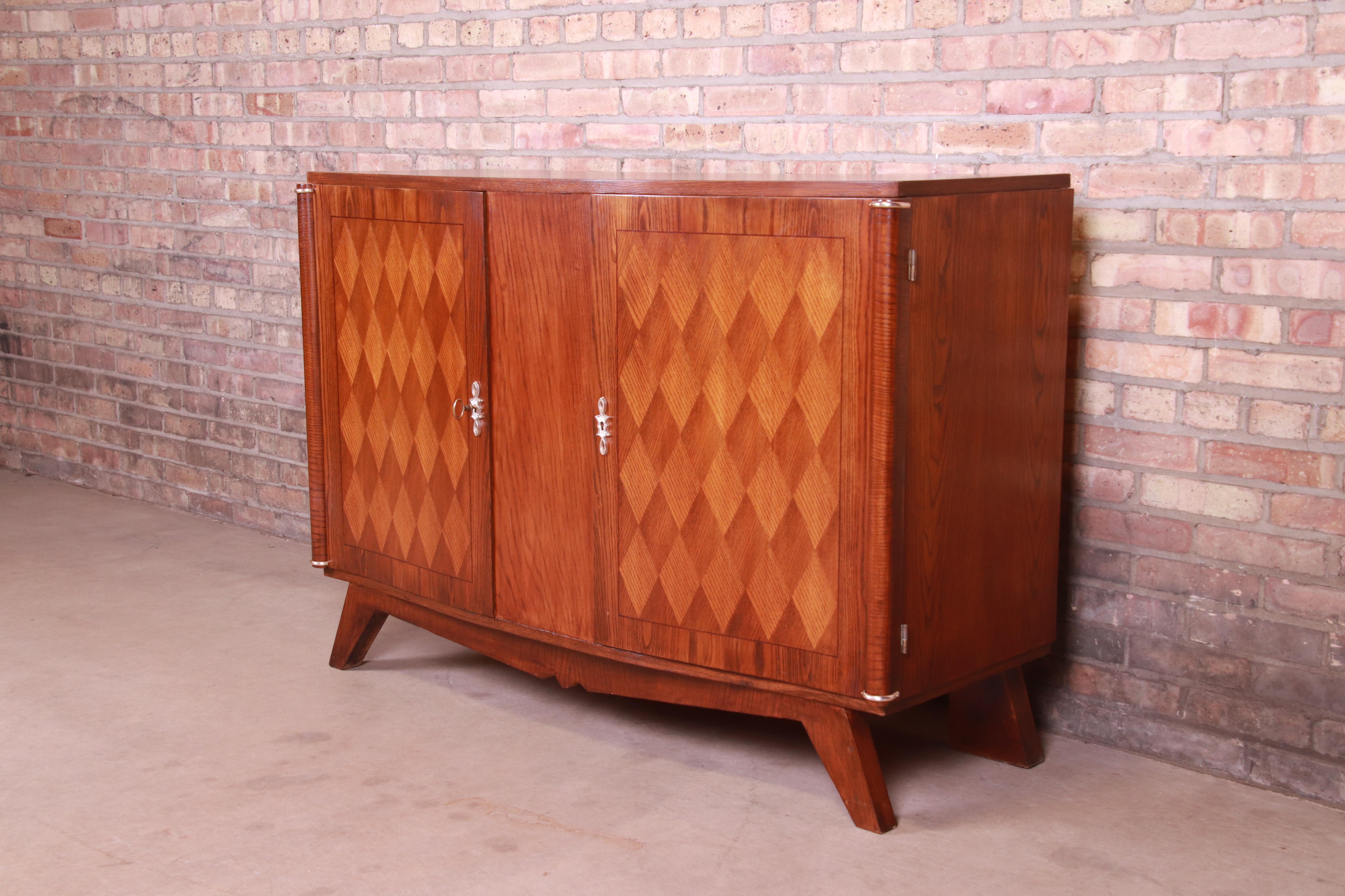 A gorgeous French Art Deco style sideboard or bar cabinet

In the manner of Jules Leleu

20th century

Carved oak, with inlaid parquetry front and original brass hardware. Cabinets lock, and key is included.

Measures: 52.5