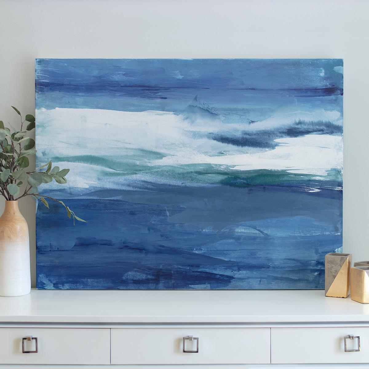 This abstract coastal painting by Julia Contacessi is made with acrylic paint on canvas. The composition, while highly abstract, is balanced - with broad, layered strokes of deep blues and thick white and a pop of muted green creating a large