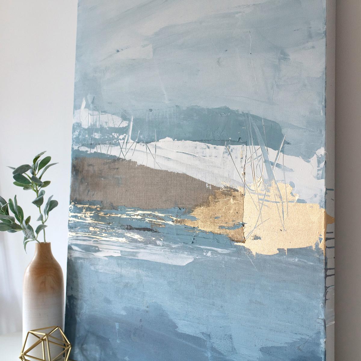 This abstract painting is made using mixed media including linen and gold. It features a cool blue and white palette, with large, expressive strokes layered over textured linen, with metallic gold adding a contrasting accent to the composition,. The
