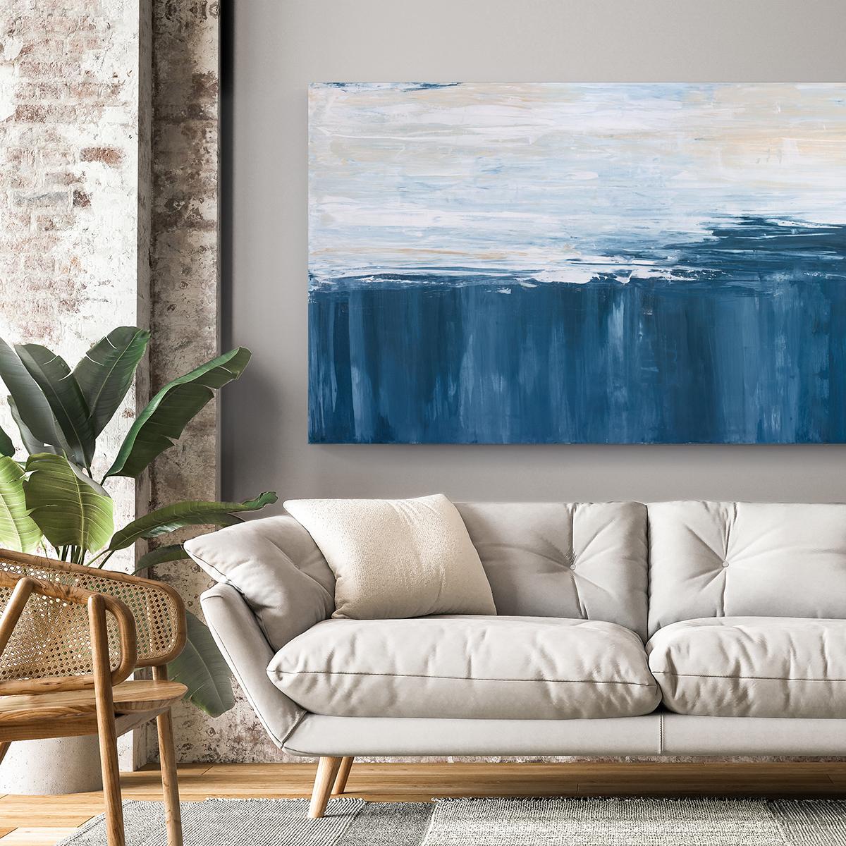 This large abstract statement painting by Julia Contacessi features a cool palette with deep blue on the bottom half of the composition, and white and neutral tones layered in strokes across the top half of the piece. This abstract painting is made