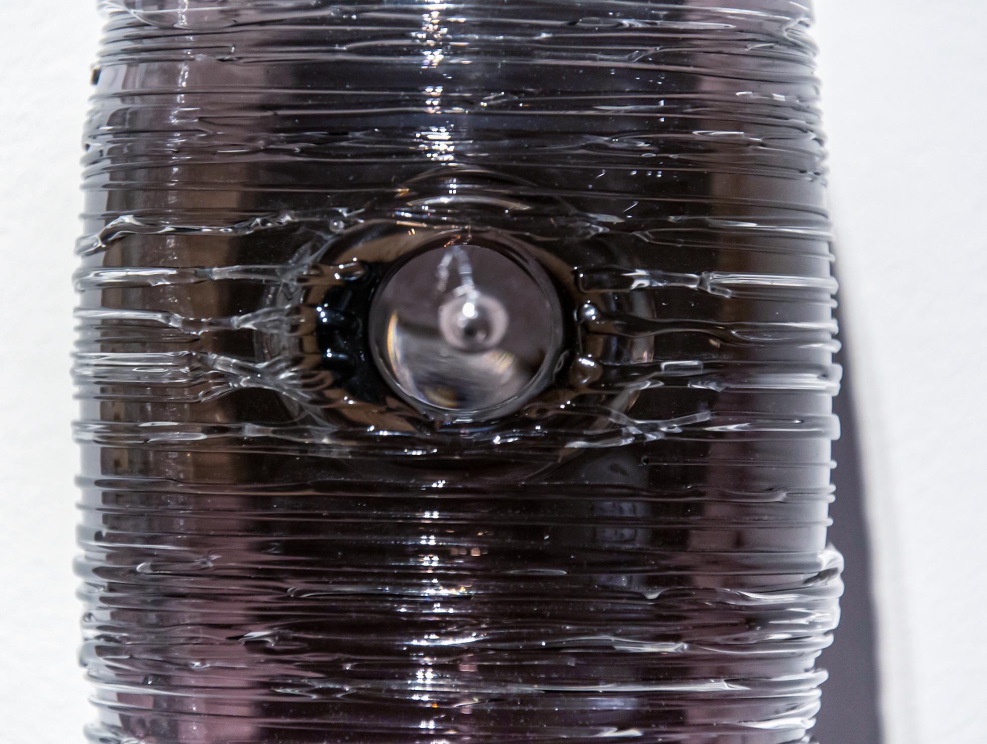 Trois formes de cocons en verre texturé transparent, gris anthracite et noir sont disposées verticalement dans cette sculpture murale unique de Julia Reimer.  Inspirés par la nature, les éléments ressemblent à des cocons ou, parce qu'ils sont chacun