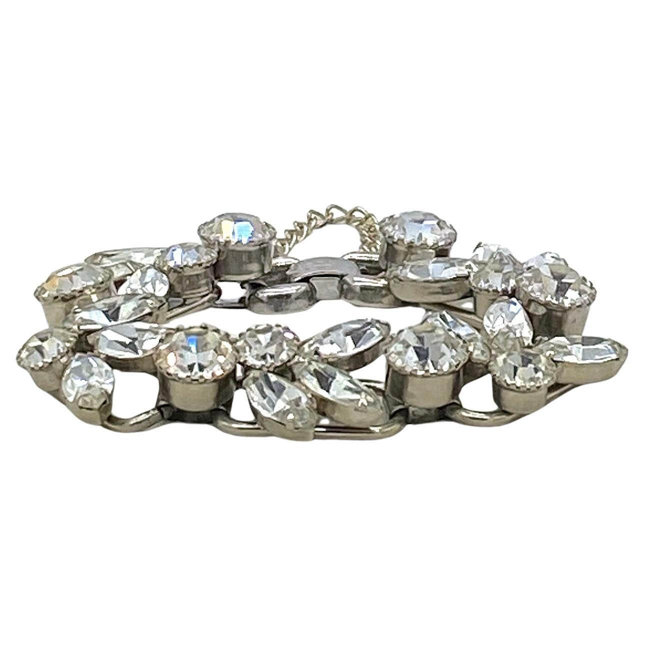 This is an identified Juliana D&E clear rhinestone bracelet. The five chaton and navette stones cluster segments are prong-set on rhodium-plated linked rings (5 ring links are their bracelet typical construction) with a security chain. This vintage