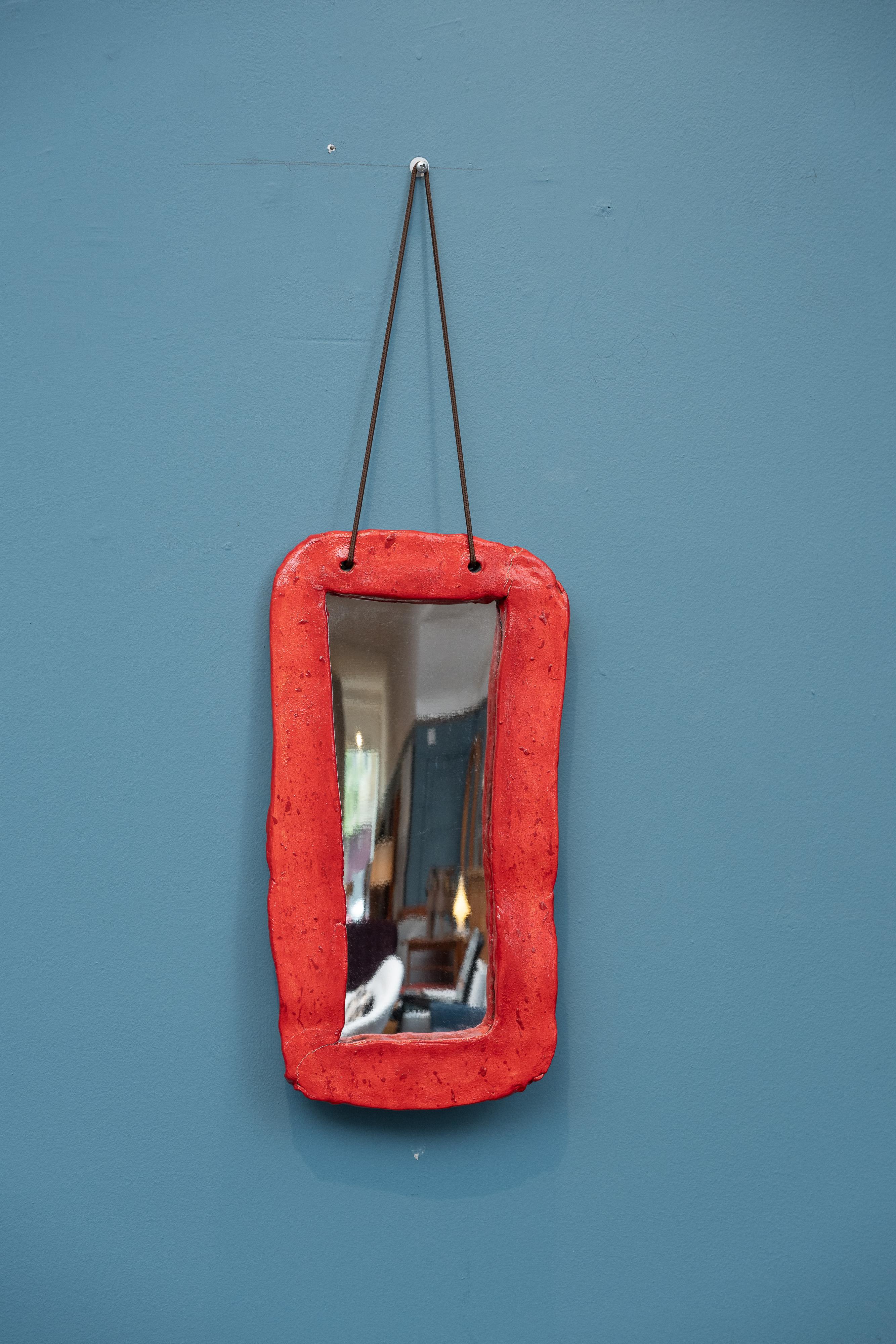 Miroir mural en céramique émaillée à la main Juliette Derel, France. Miroir asymétrique fait à la main, signé, avec cordon de suspension d'origine. Un design accrocheur dans un glaçage rouge vibrant, parfait pour une entrée ou un petit coin. Le