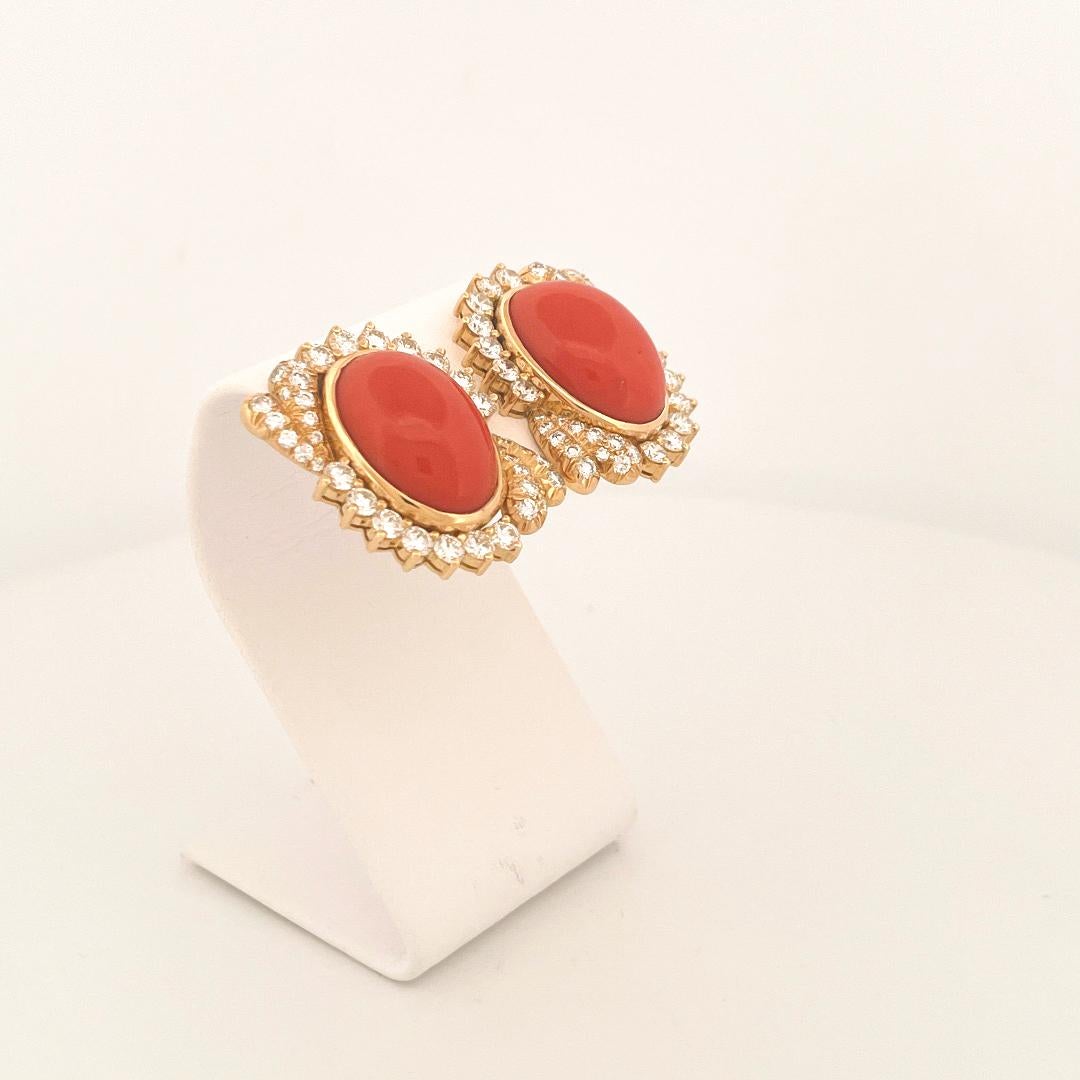From designer Julius Cohen, circa 1970s, 18 karat yellow gold coral and diamond earrings. These earrings are crafted with 2 center bezel set cabochon cut coral stones with a combined weight of 20.24 carats. Additionally, surrounding the coral