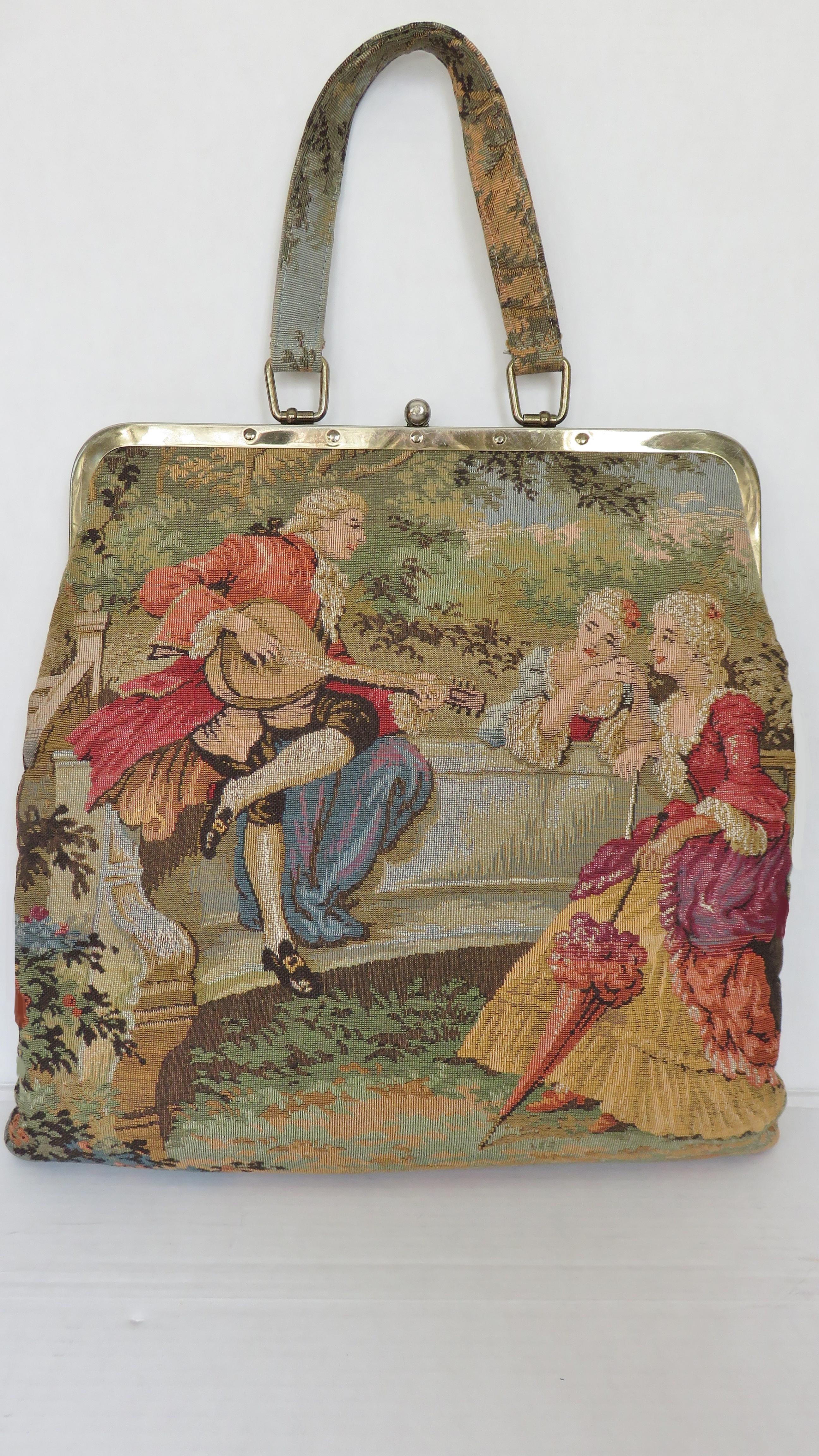 A beautiful large tapestry handbag from JR Julius Resnick.  It has a top handle and a hinged frame with top clasp. One side is pictured with an 18th century man and woman dancing and on the other a man treating 2 women to an instrumental serenade.