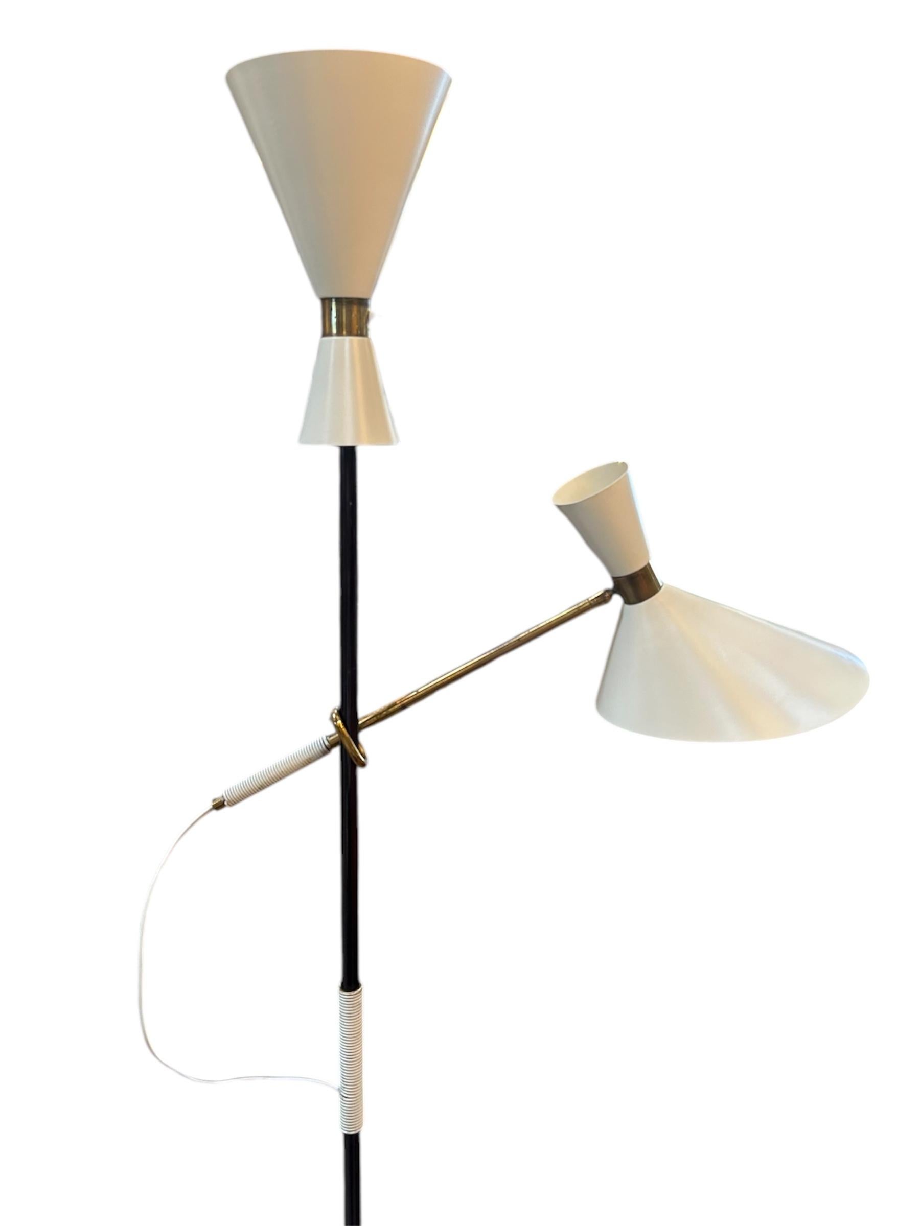 This rare floor lamp, known as the Pelican model, was designed by Julius Theodore Kalmar in 1950. It features a sculptural black metal stem, dual conical shades in cream-white, and elegant brass accents. Offering both uplighting and directional task