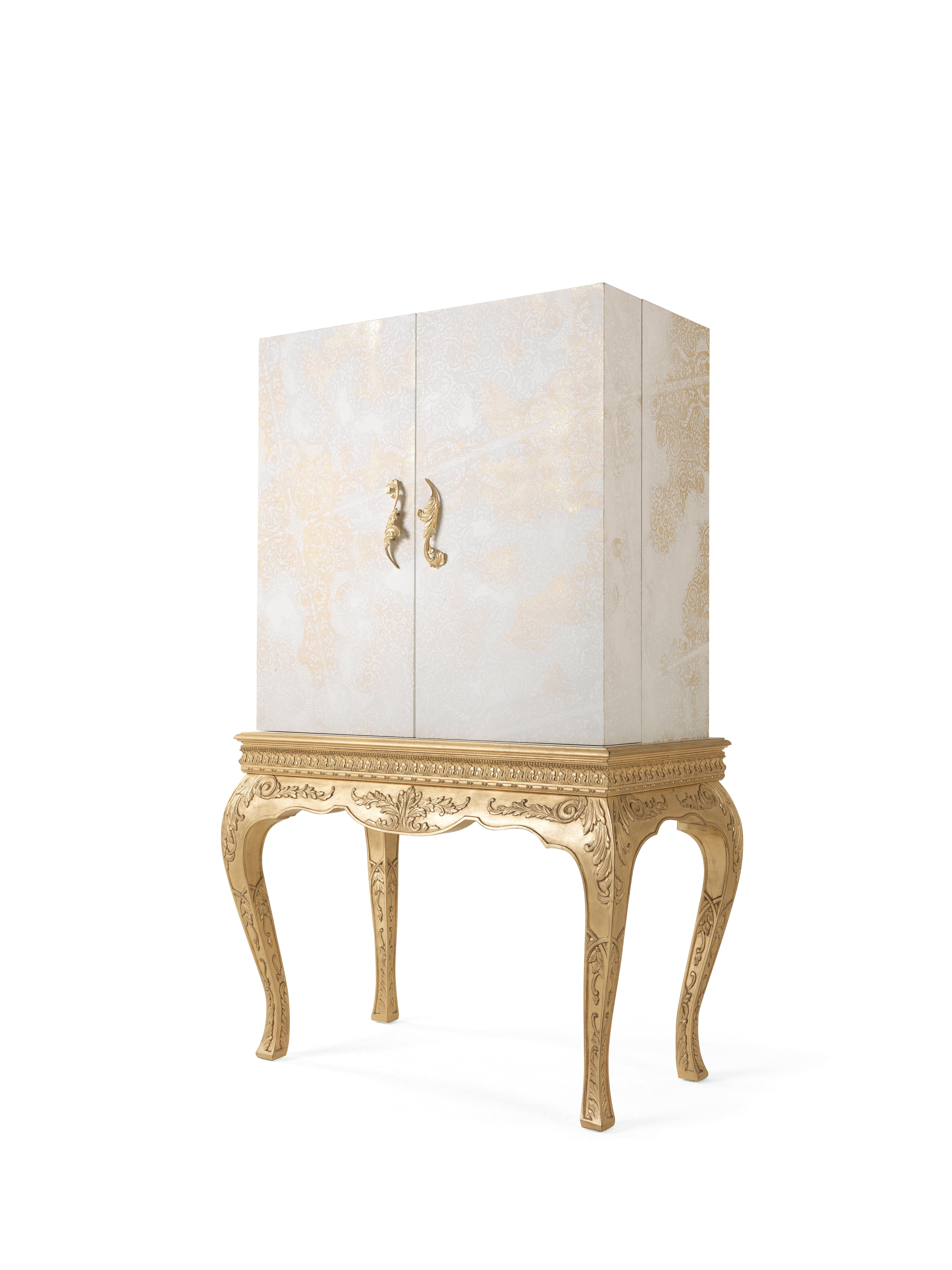 The jewel cabinet of the Brocart line presents a base with hand-carved legs and antique gold leaf finishing in pure classic style, combined with an upper part featuring a more essential and linear volume. The ornamental theme evokes the Cantù lace,