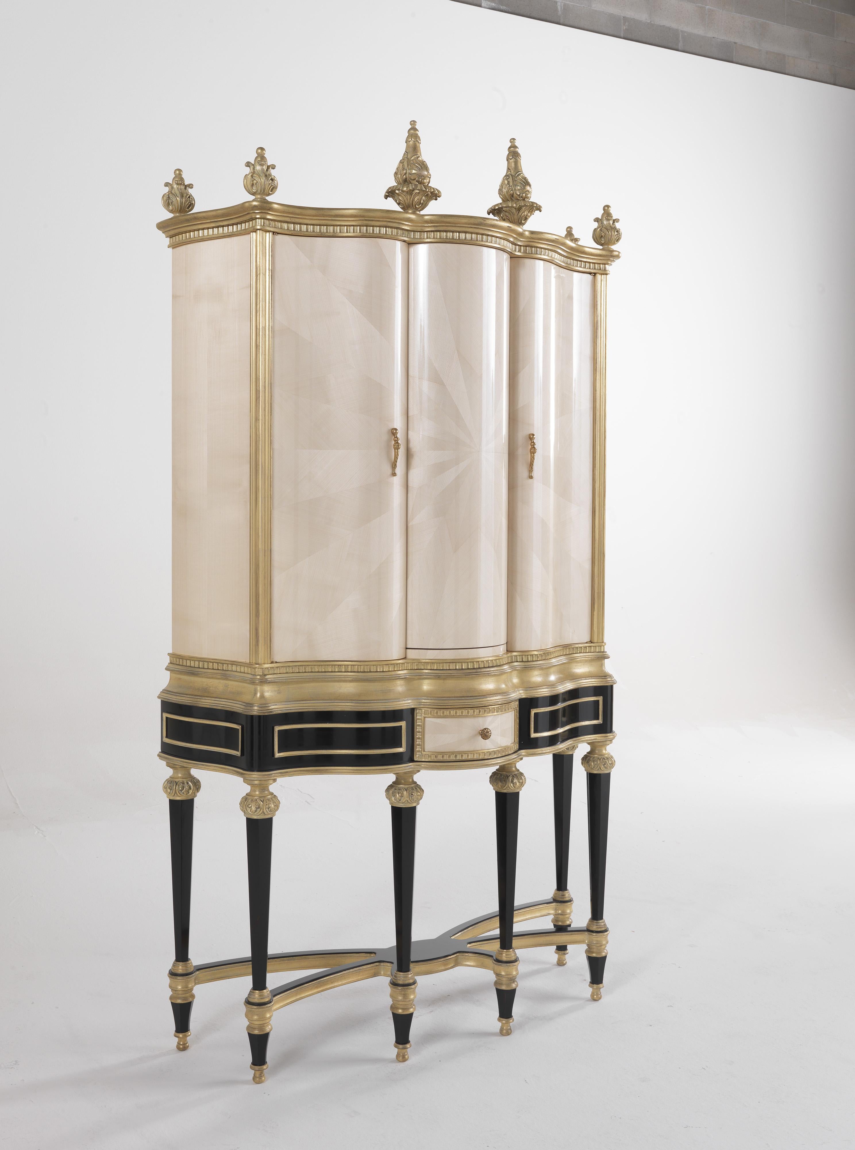 HImpactful and impressive, Hypnos bar unit with external finishing in maple with sunburst carvings and antique gold-plating, features a special mechanism that synchronizes the opening of the lateral doors with the rotation of the central part,