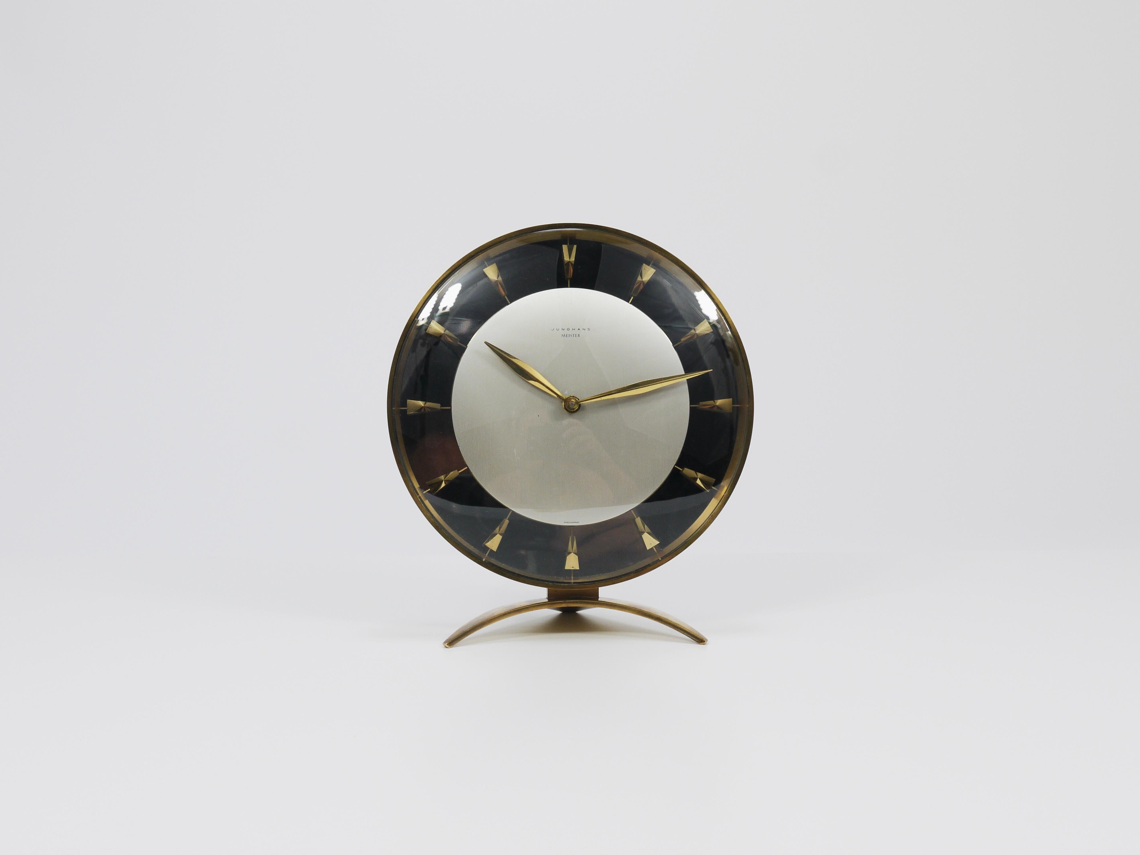 An elegant and exquisite Mid-Century Modern desk or table clock with a mechanical 8-day movement from the 1950s. Designed and manufactured by Junghans in Germany. This stunning clock features a brass housing and stands on a gracefully curved tripod