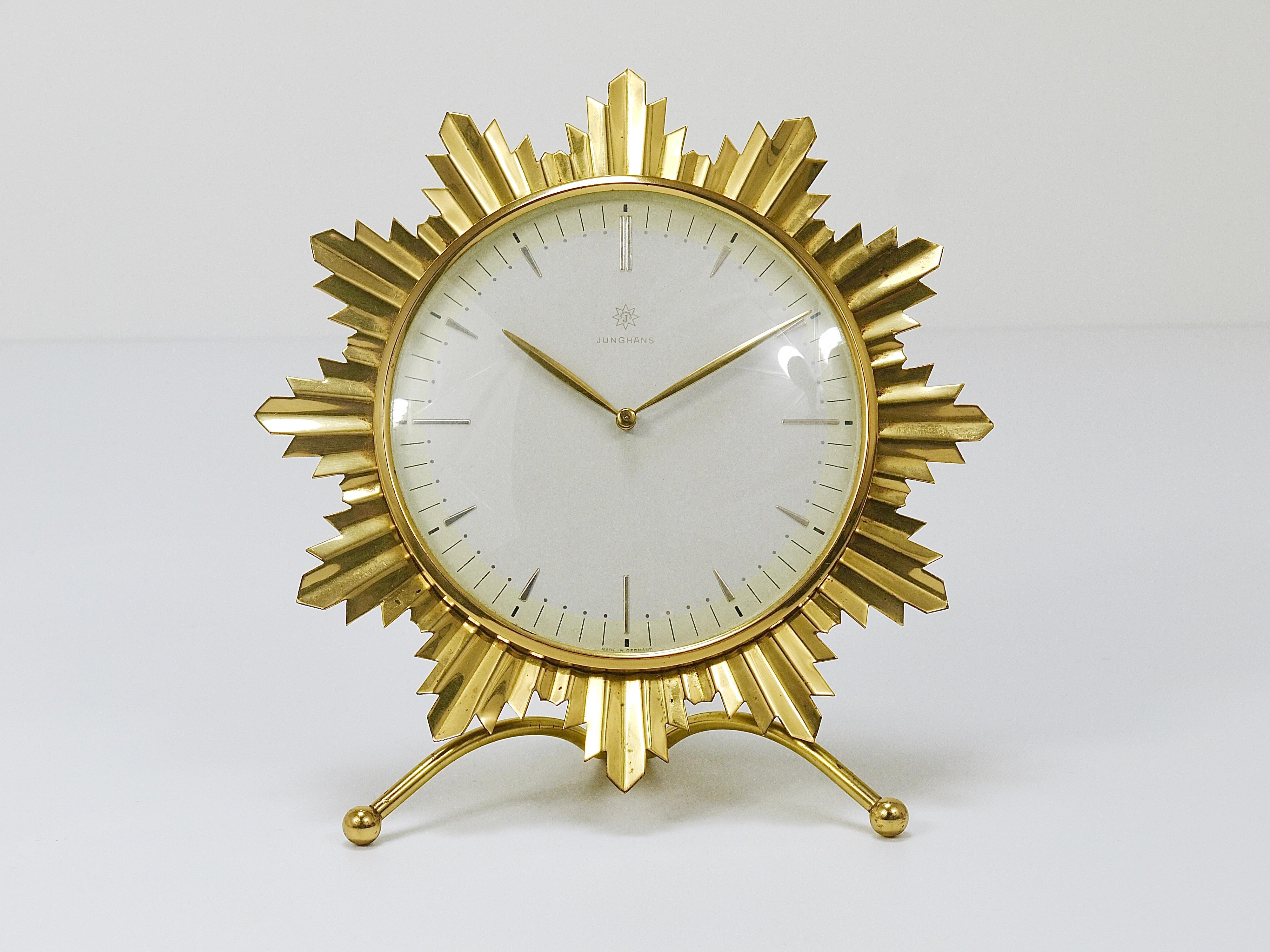 A wonderful Atomic Starburst Hollywood Regency table or desk clock from the 1950s, executed by Junghans Germany. The clock has a beautiful withe and pastel yellow clocks face with golden hands and indices and a nice sunburst brass frame. The clock