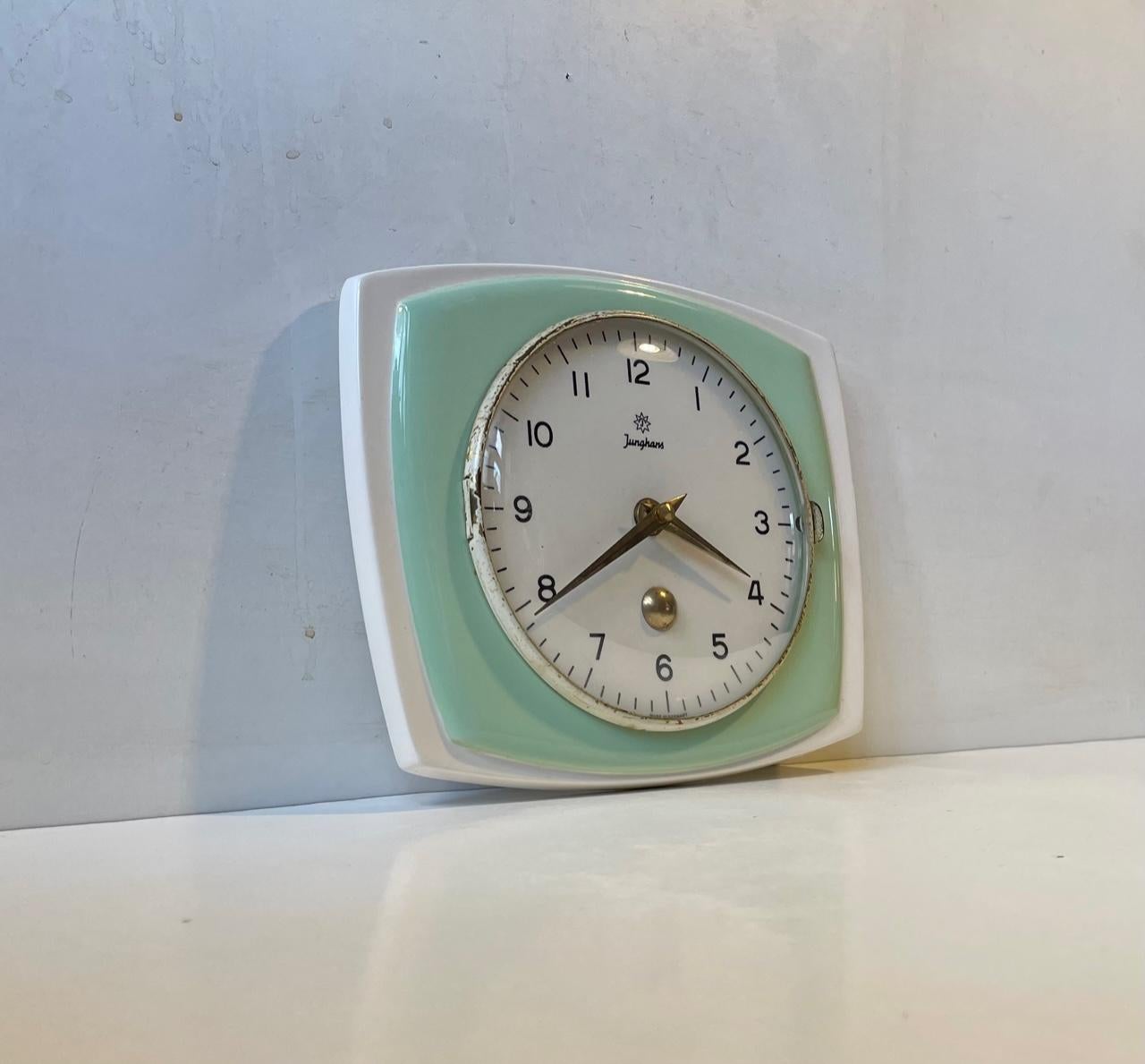 A midcentury German porcelain wall clock decorated with pastel green glaze. It features a slightly concave glass front that can be opened sideways. Made by Junghans in West Germany circa 1950-60. It is operated by a quartz movement. Measurements: