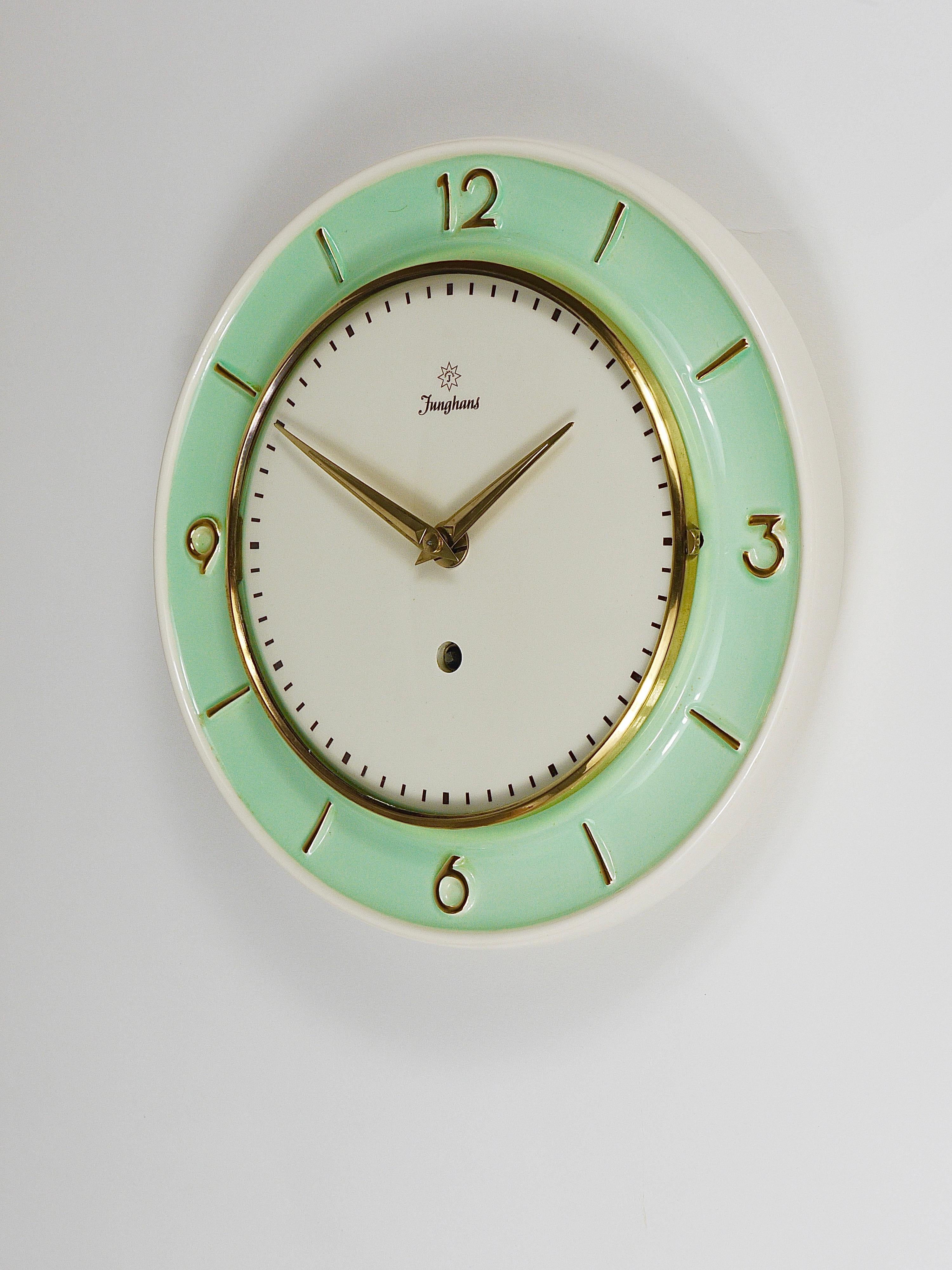 A lovely round turquoise mid-century wall clock, crafted by Junghans in Germany during the 1950s. Designed in the characteristic style of the era, it features elegant brass hands, a brass frame with domed glass, and a white & light green / mint