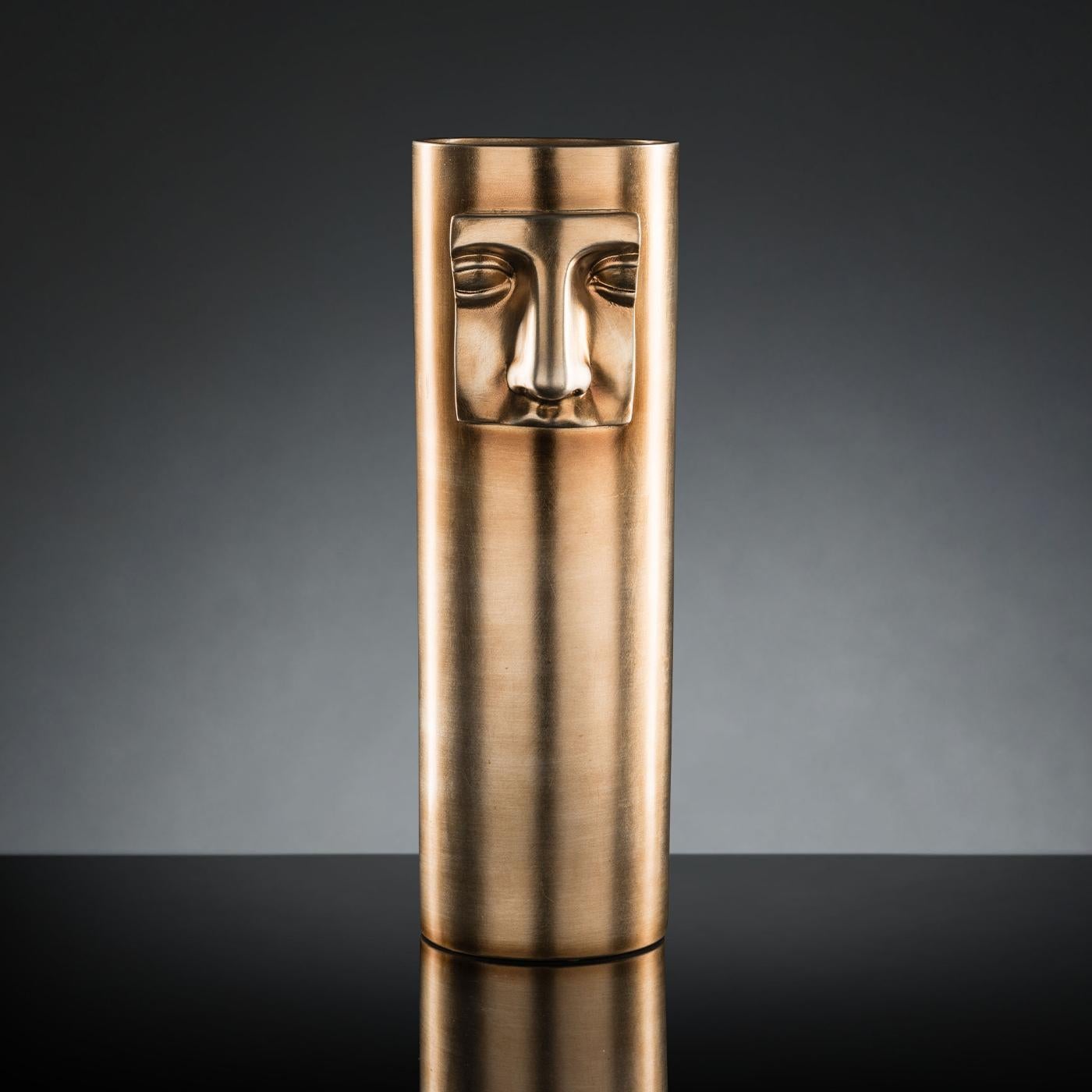 This exquisite decorative vase will infuse a contemporary living room or entryway with a unique and sophisticated aura. Superbly handcrafted of ceramic and finished in a metallic brass color, this cylindrical piece is enriched with a striking low