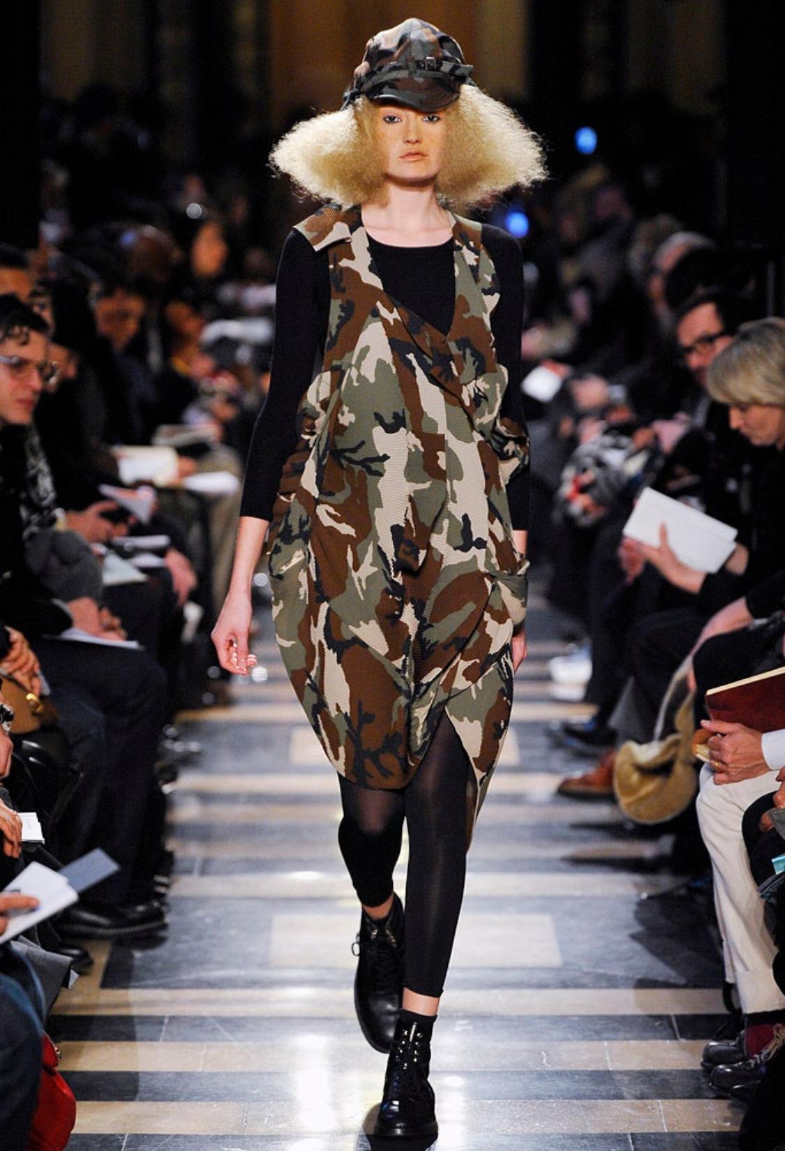 The Junya Watanabe Comme des Garçons AW 2010 Runway Green Camo Print Pleated Asymmetrical Dress is a striking and innovative piece that embodies the essence of avant-garde fashion. Crafted in Japan, this dress showcases a unique pleated design that