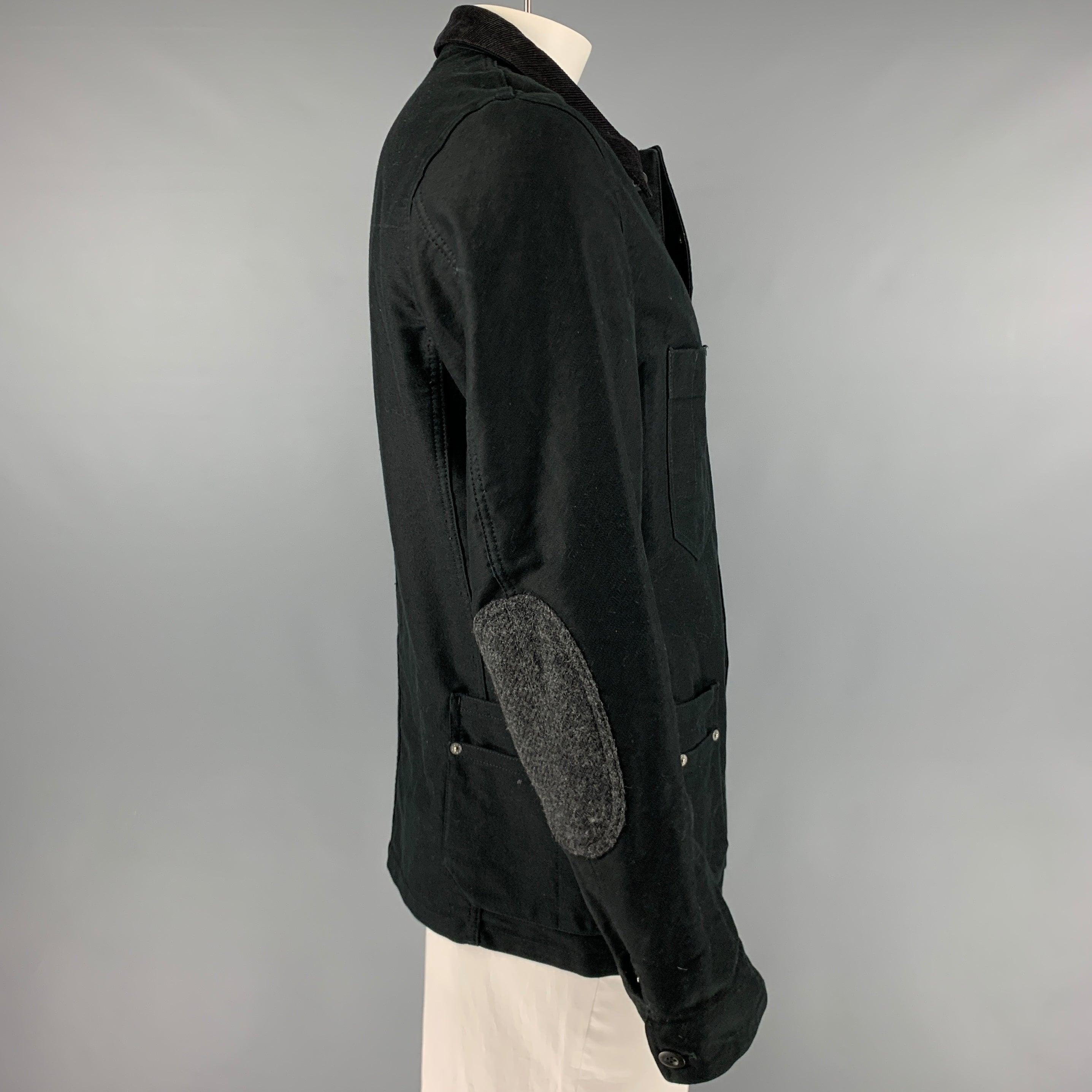 JUNYA WATANABE jacket
in a black cotton fabric featuring a worker style with multiple utilitarian pockets, leather pocket detail, ribbed collar, elbow patches, and button closure. Made in Japan.Excellent Pre-Owned Condition. Minor marks on button