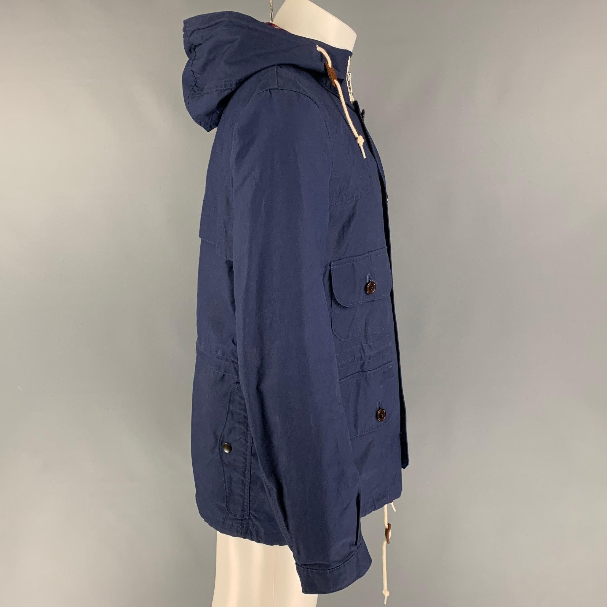 Die Jacke von JUNYA WATANABE aus beschichtetem Segeltuch in Marineblau mit kariertem Besatz hat einen maritimen Stil, braune Cordbesätze, aufgesetzte Taschen, Kordelzug, Kapuze, Steppnähte und einen Reißverschluss mit Knöpfen. Hergestellt in