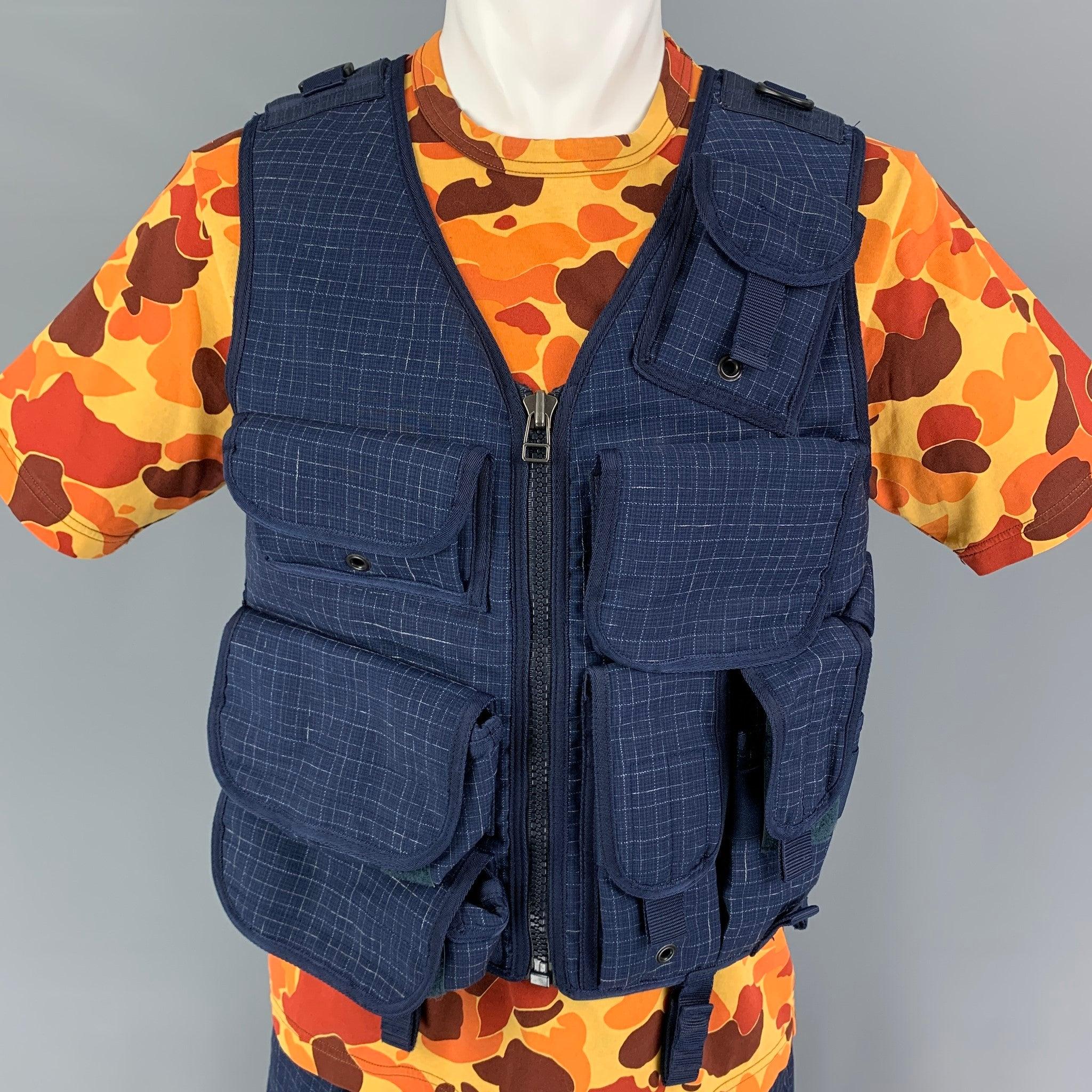 JUNYA WATANABE x Ark Air SS19 3 Piece Set comes in a blue checked print mixed materials with a camouflage print interior utility vest featuring hook & loop shoulder straps, 8 flap pockets, three internal pockets, metal eyelets, side adjusters, zip