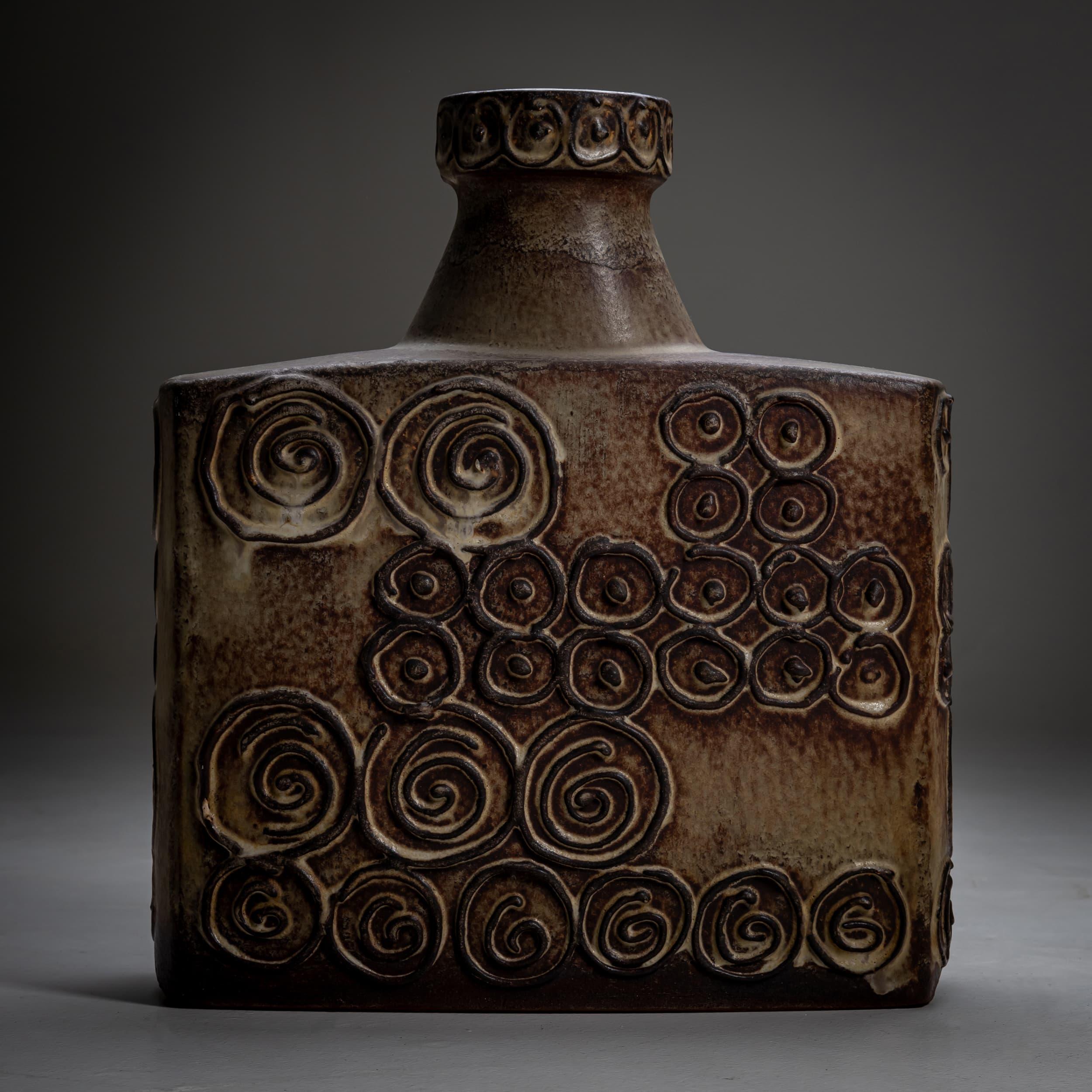 Jarrón de cerámica marrón del Jura, del fabricante alemán occidental Scheurich, de mediados del siglo XX. El jarrón presenta un cuerpo rectangular adornado con motivos en espiral y un cuello corto y estrecho. La base está marcada con 