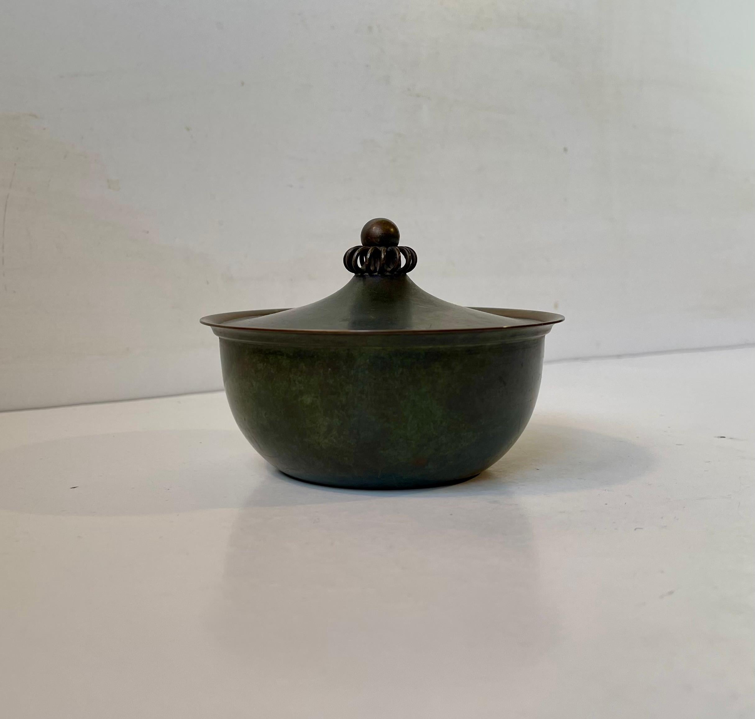 Early green patinated jar or trinket in bronze designed by Just Andersen and manufactured in the early 1930s. Ornate Josef Frank inspired handle to the lid. Fully signed and numbered to its base. Measurements: D: 11 cm, H: 8 cm. Small dent to the