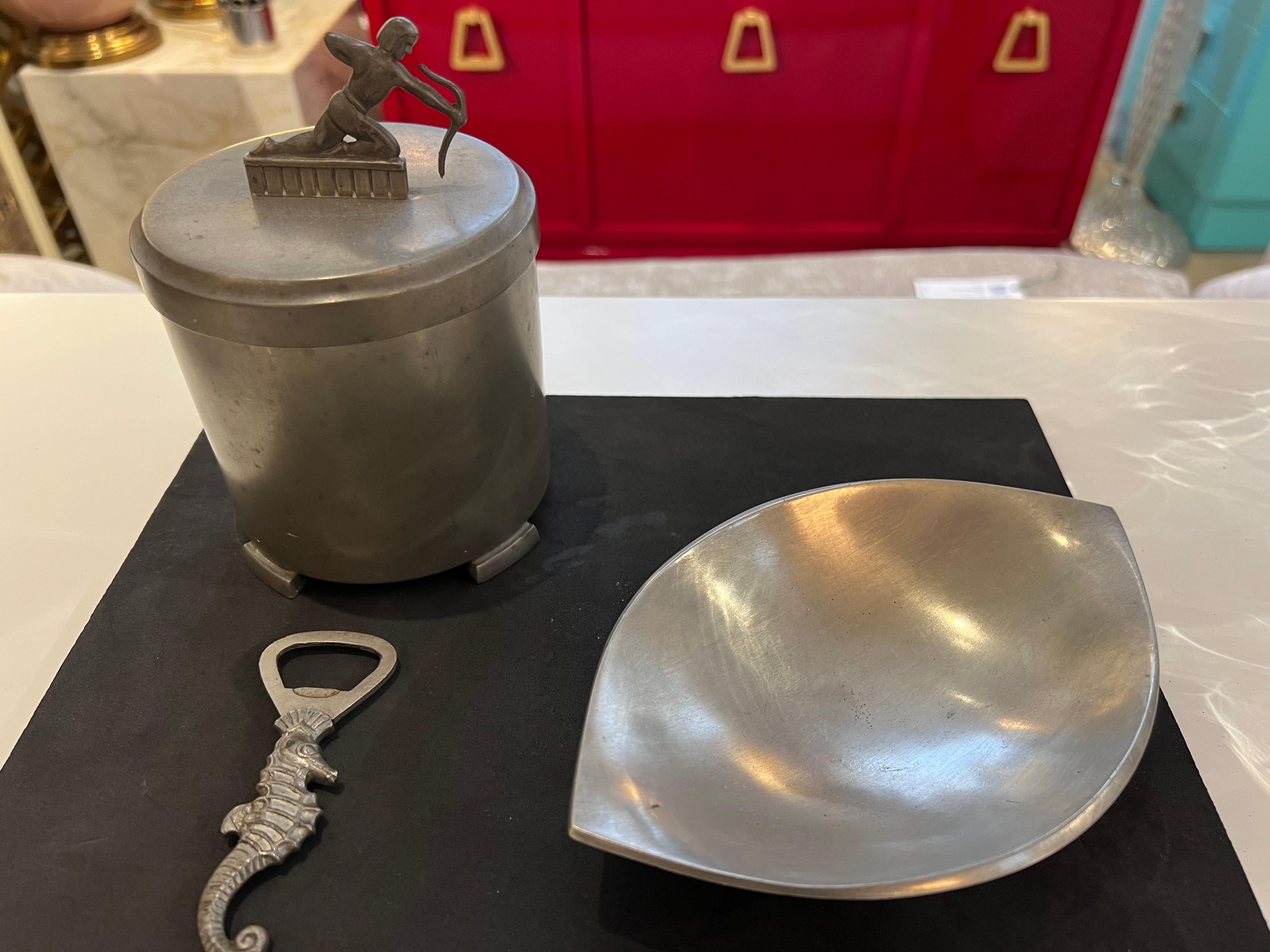 A great set of 3 decorative pewter pieces by Danish maker, Just Andersen. One is a jar canister, can be used in a bathroom to hold cotton or q tips. The lid is decorated with a crouched archer. Another is a dish which can be used for soap. The other