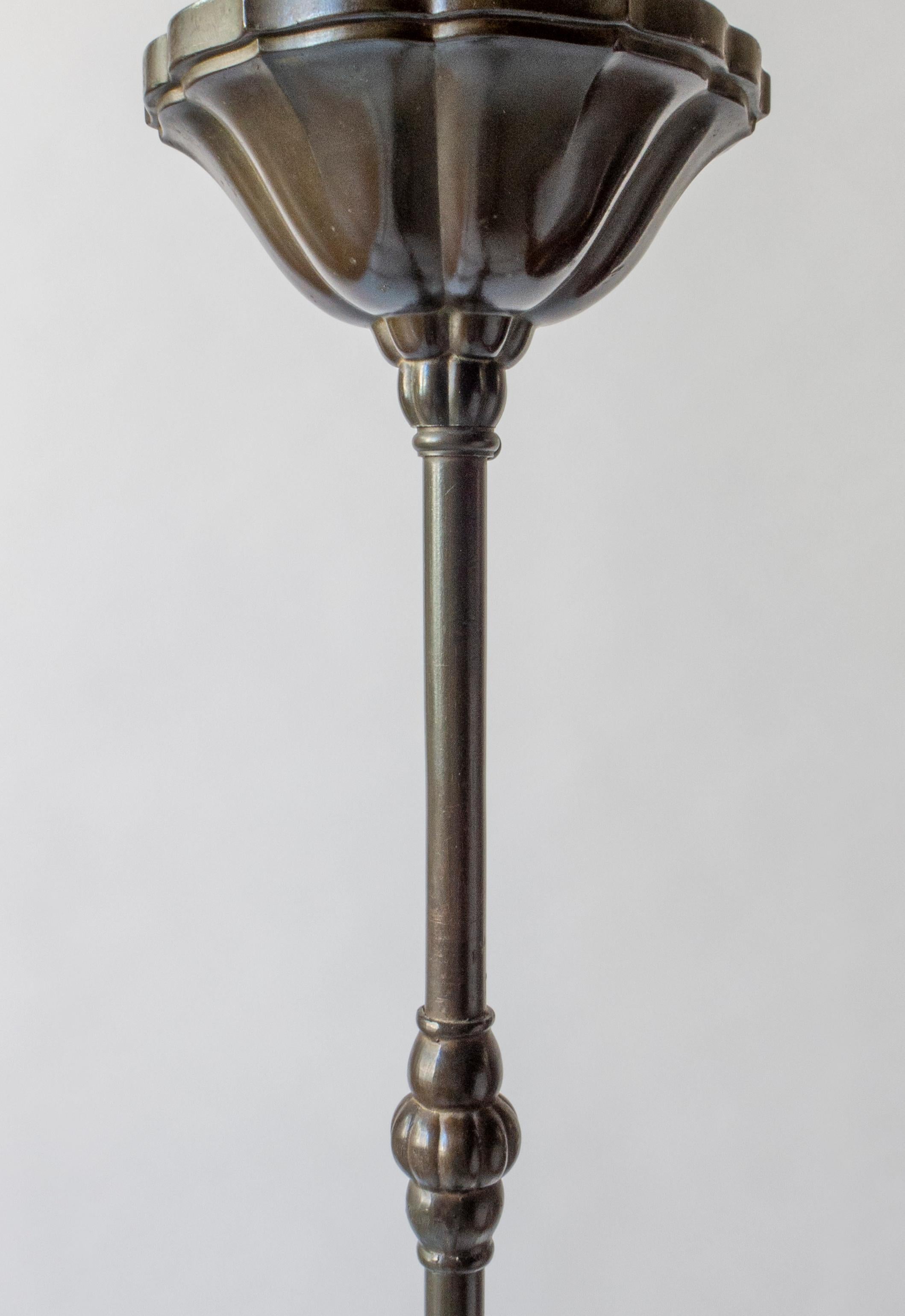The scalloped canopy, above a bisected hanging rod with bun-form fastener, the gourd shaped body sprouting three C-shaped arms, each arm surmounted by a glass sheathed light holder, terminating in a cone shaped finial. Marked on the interior of the