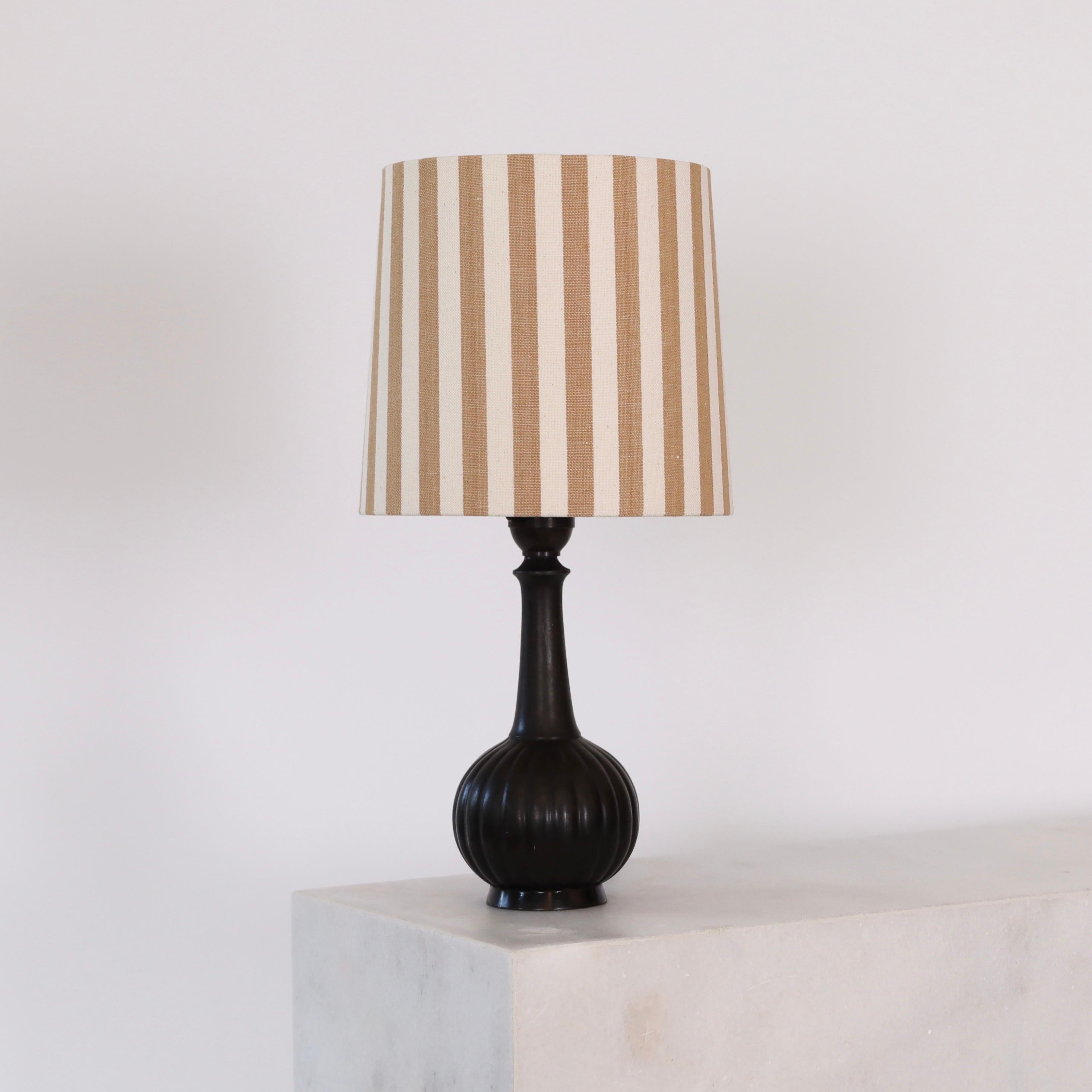 Lampada da scrivania Just Andersen del 1920 con paralume in tessuto a righe. Un piccolo pezzo di storia per un bellissimo spazio. 
 
* Una lampada da tavolo in metallo con una base rotonda a linee verticali e un paralume in tessuto a righe color