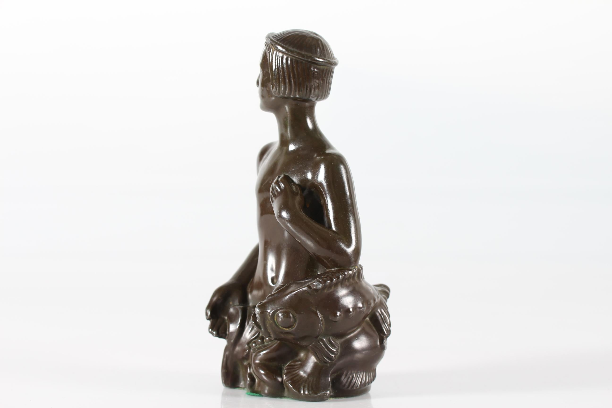 Statuetta originale disegnata dall'artista e scultore danese Just Andersen (1884-1943) che raffigura un giovane uomo con un pesce.
È stata realizzata in Danimarca negli anni '40-'50 con il metallo da discoteca creato da Just Andersen con una patina