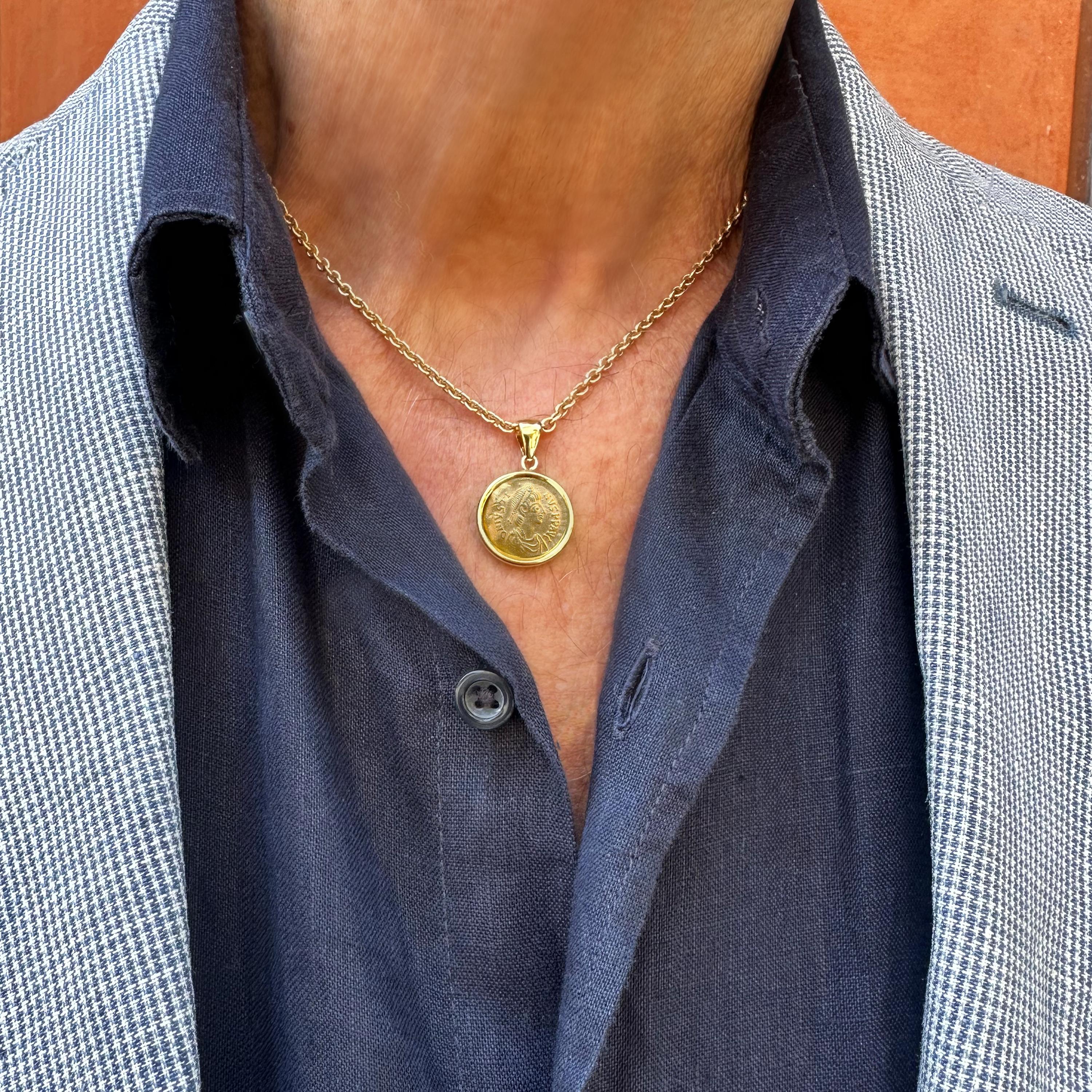 This exquisite 18Kt gold pendant houses a 24Kt gold Byzantine coin (Tremissis) from the 6th century AD. On the obverse, it features the diademed bust of Emperor Justin I, while on the reverse, Victory is depicted advancing, holding a crown and a