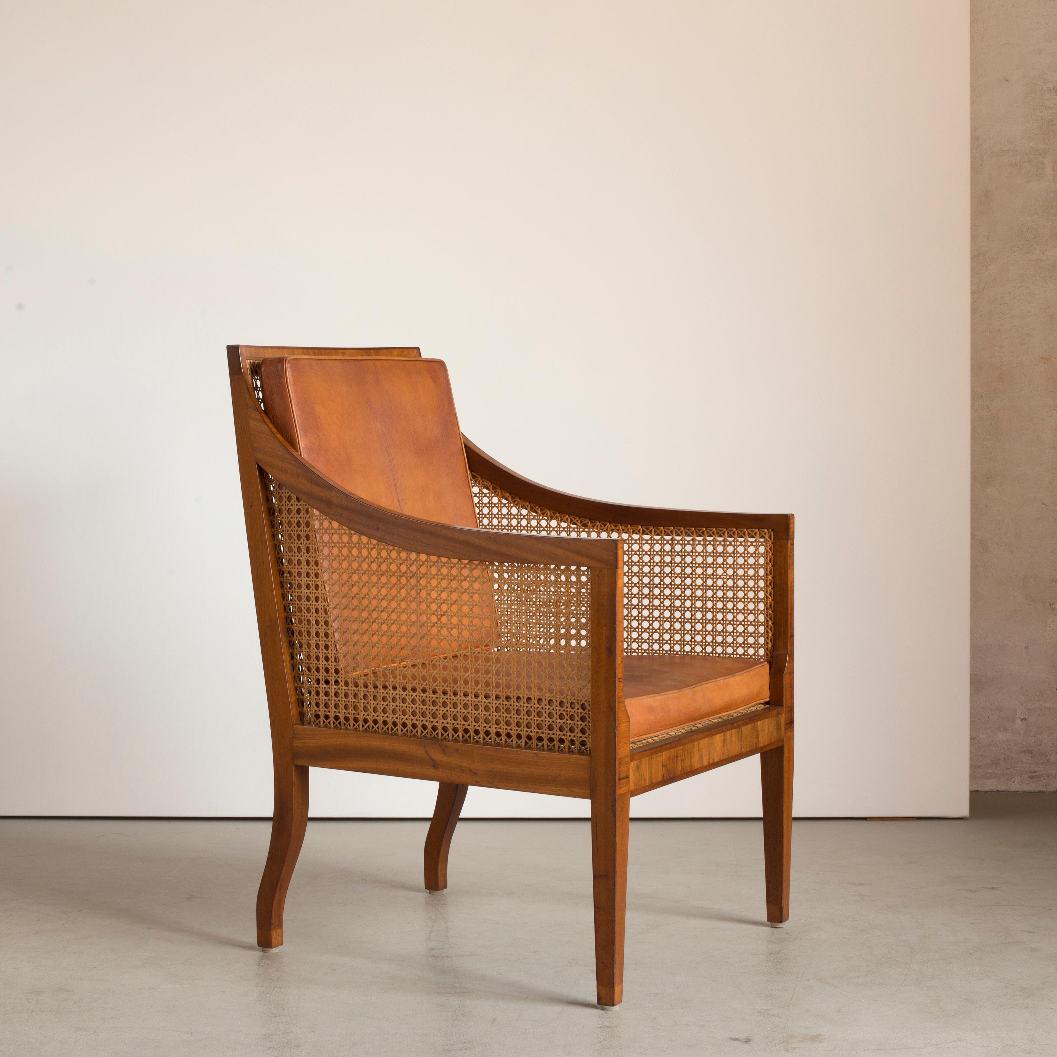 Kaare Klint Bergere of Mahogany. Sides, seat and back with woven cane. Loose cushions in seat and back upholstered with patinated niger leather. Executed by Rud. Rasmussen Cabinetmakers.

Reverse with paper label ‘Rud.