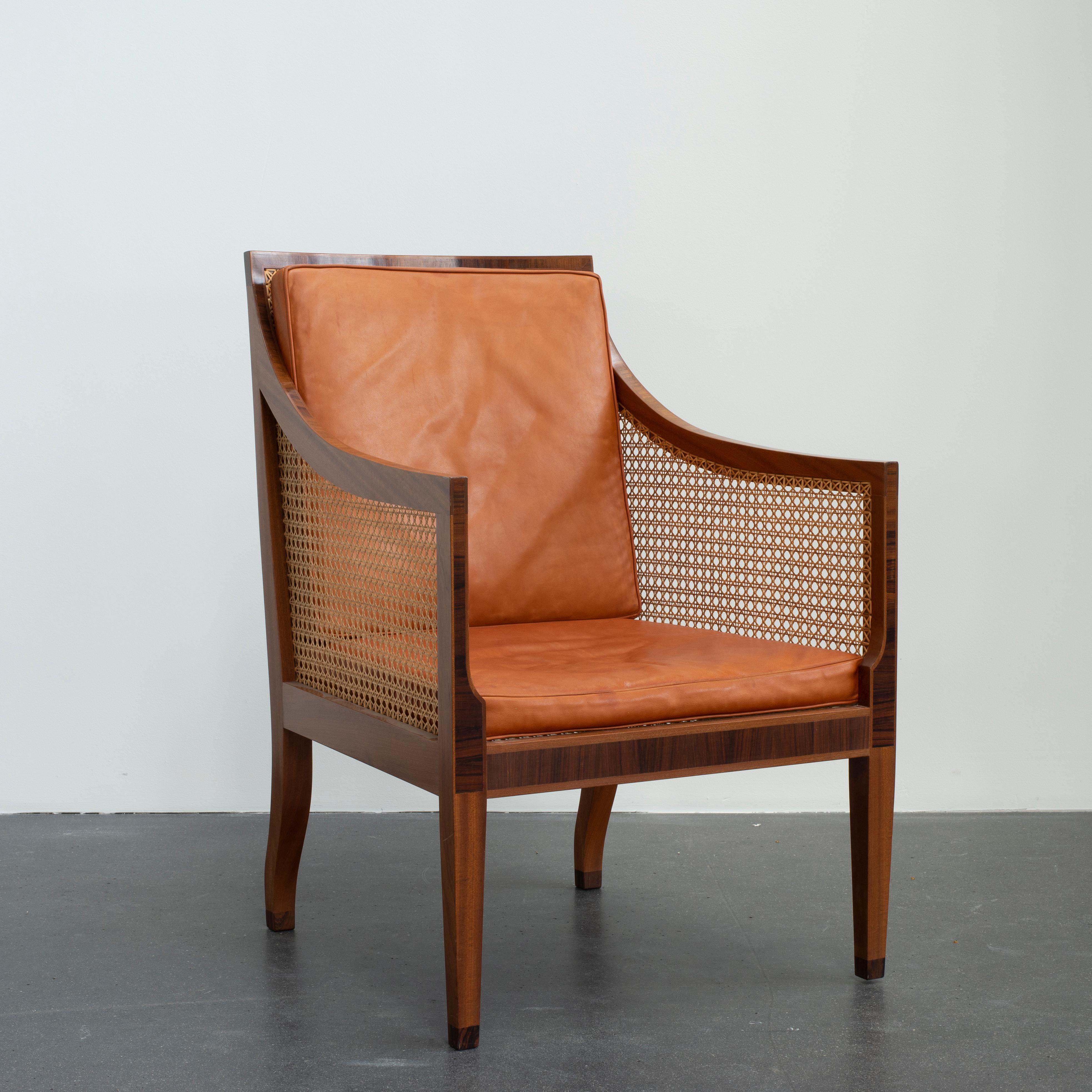 Kaare Klint bergere of mahogany. Sides, seat and back with woven cane. Loose cushions in seat and back upholstered with patinated leather. Executed by Rud. Rasmussen cabinetmakers.