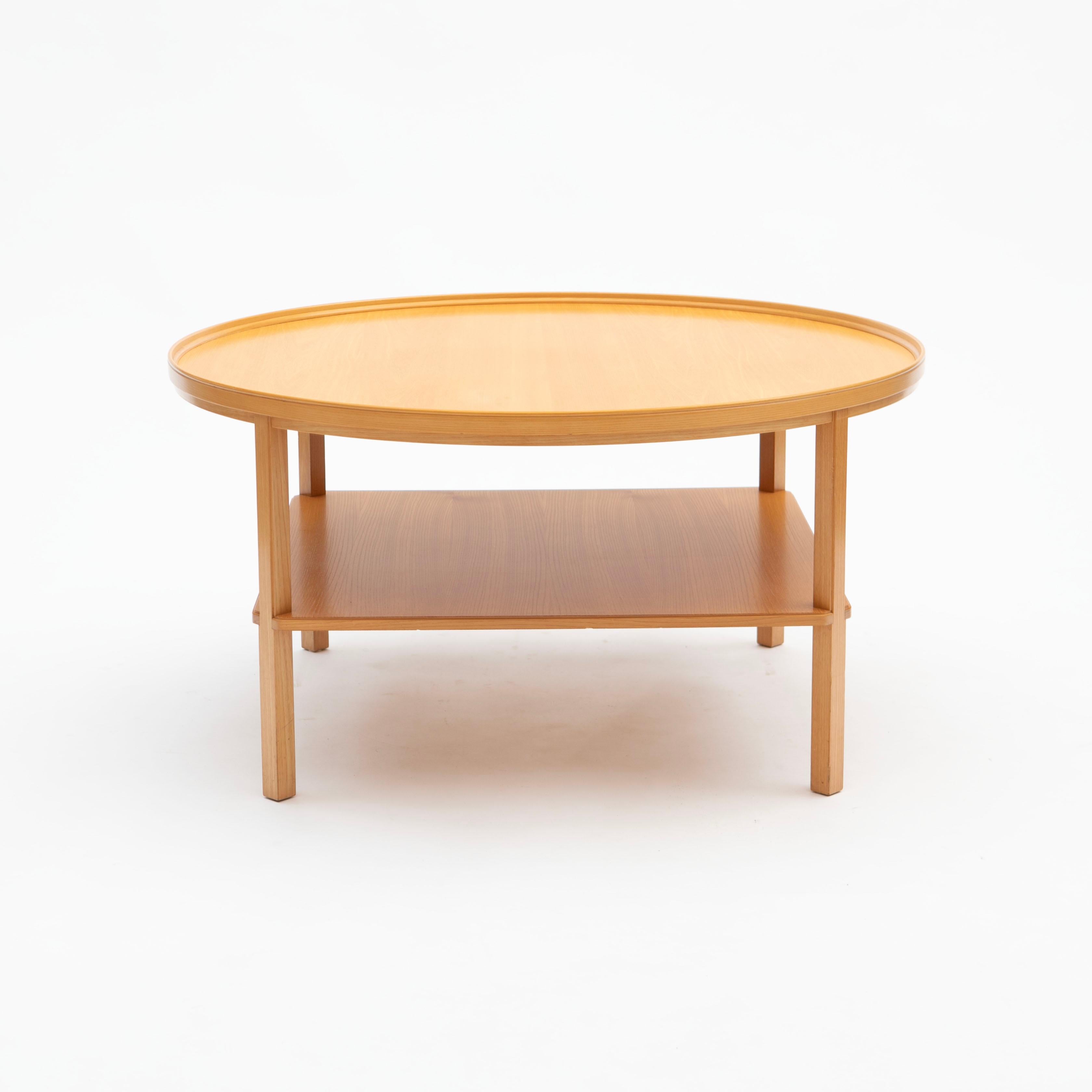 Kaare Klint 1888 - 1954.
Round coffee table, “Rygebord” model KK6687, made in ash wood with a very beautiful grain. The table features an elegant, raised band that wraps around the tabletop with a functional shelf below, supported by slightly angled