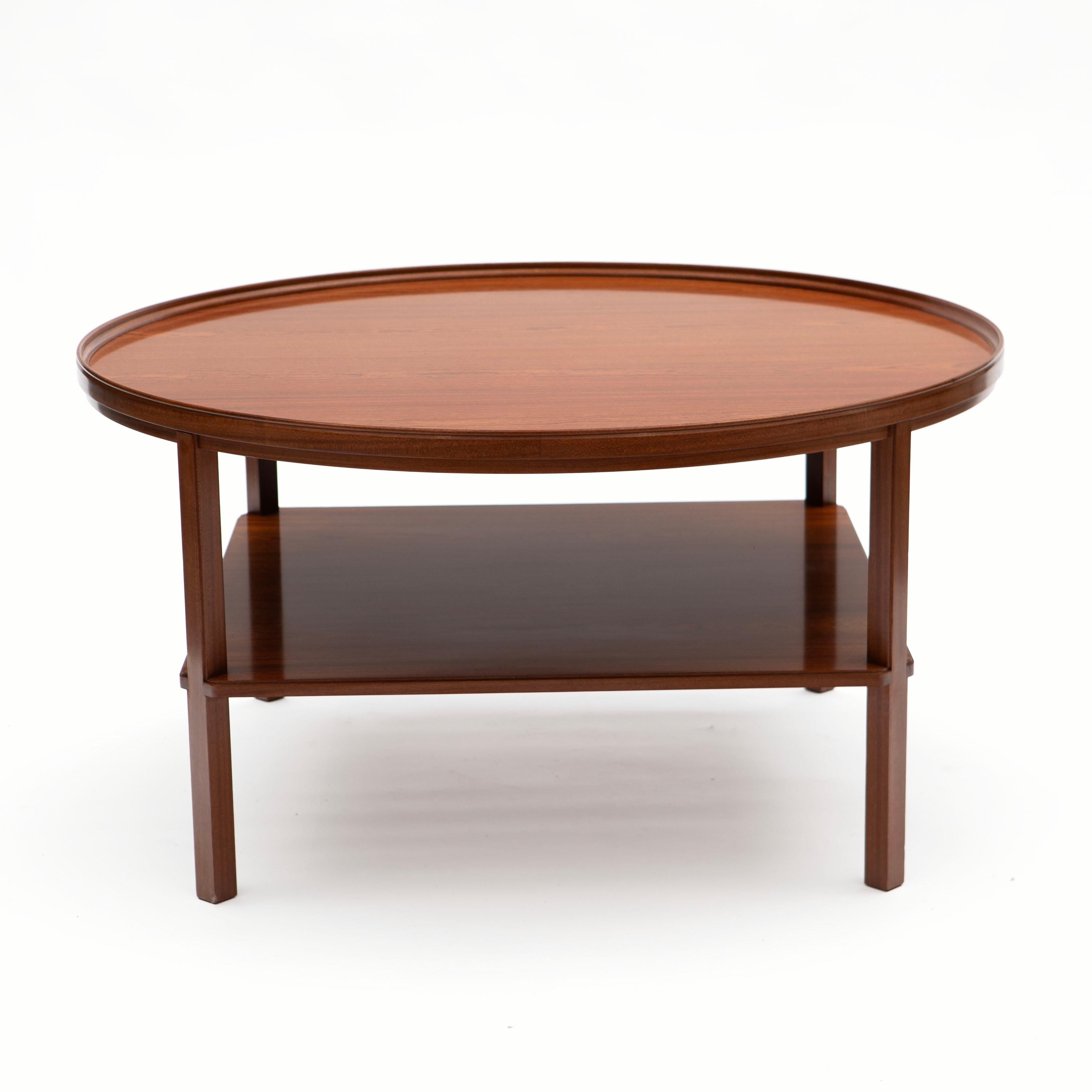 Kaare Klint 1888 - 1954.
Round coffee table, “Rygebord” model KK6687, made in mahogany with beautiful grain. The table features an elegant, raised band that wraps around the tabletop with a functional shelf below, supported by slightly angled legs.