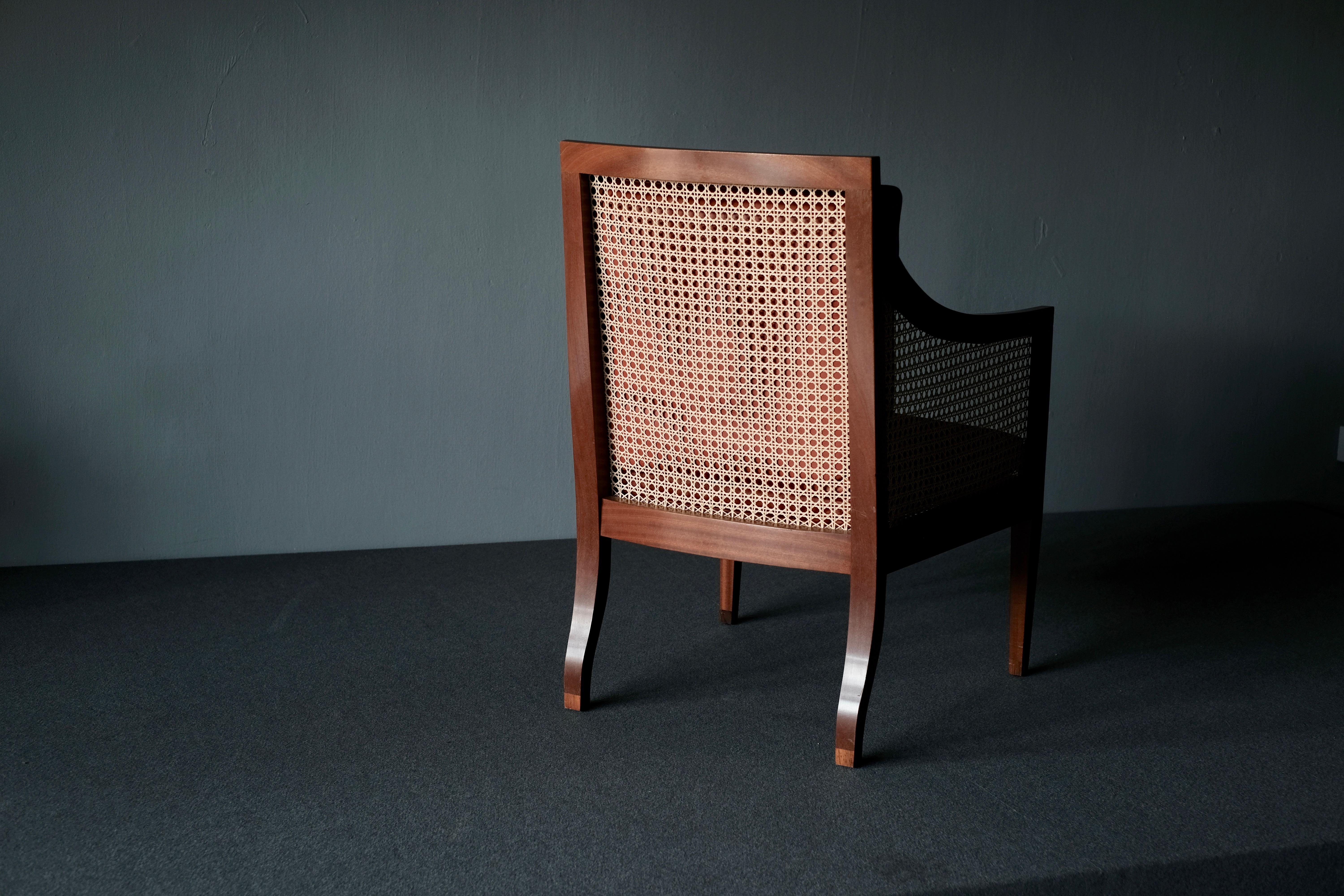 Really beautiful and elegant Kaare Klint easy chair designed in 1932 and produced by Rud. Rasmussens, Denmark. This bergère, model 4488 is in mahogany and has lovely rosewood veneers with hand woven cane sides, seat and back. The loose cushions are