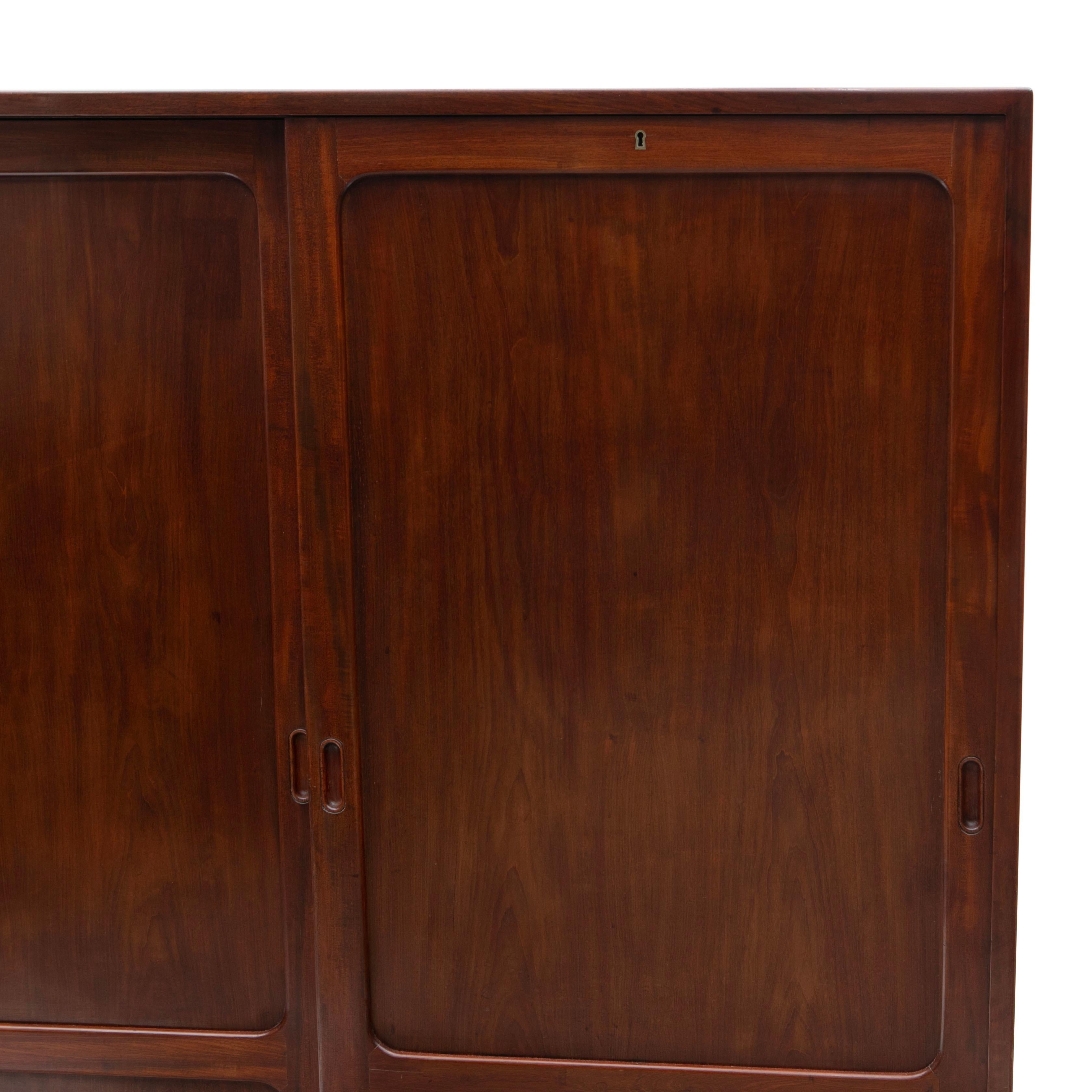 Kaare Klint, 1888-1954
Aus massivem kubanischem Mahagoni gefertigter Füll- oder Büroschrank mit zwei Schiebetüren mit leichtgängigem Schiebemechanismus, die sich zu mehreren Einlegeböden öffnen lassen. Auf einem Sockel aus Palisanderholz ruhend,