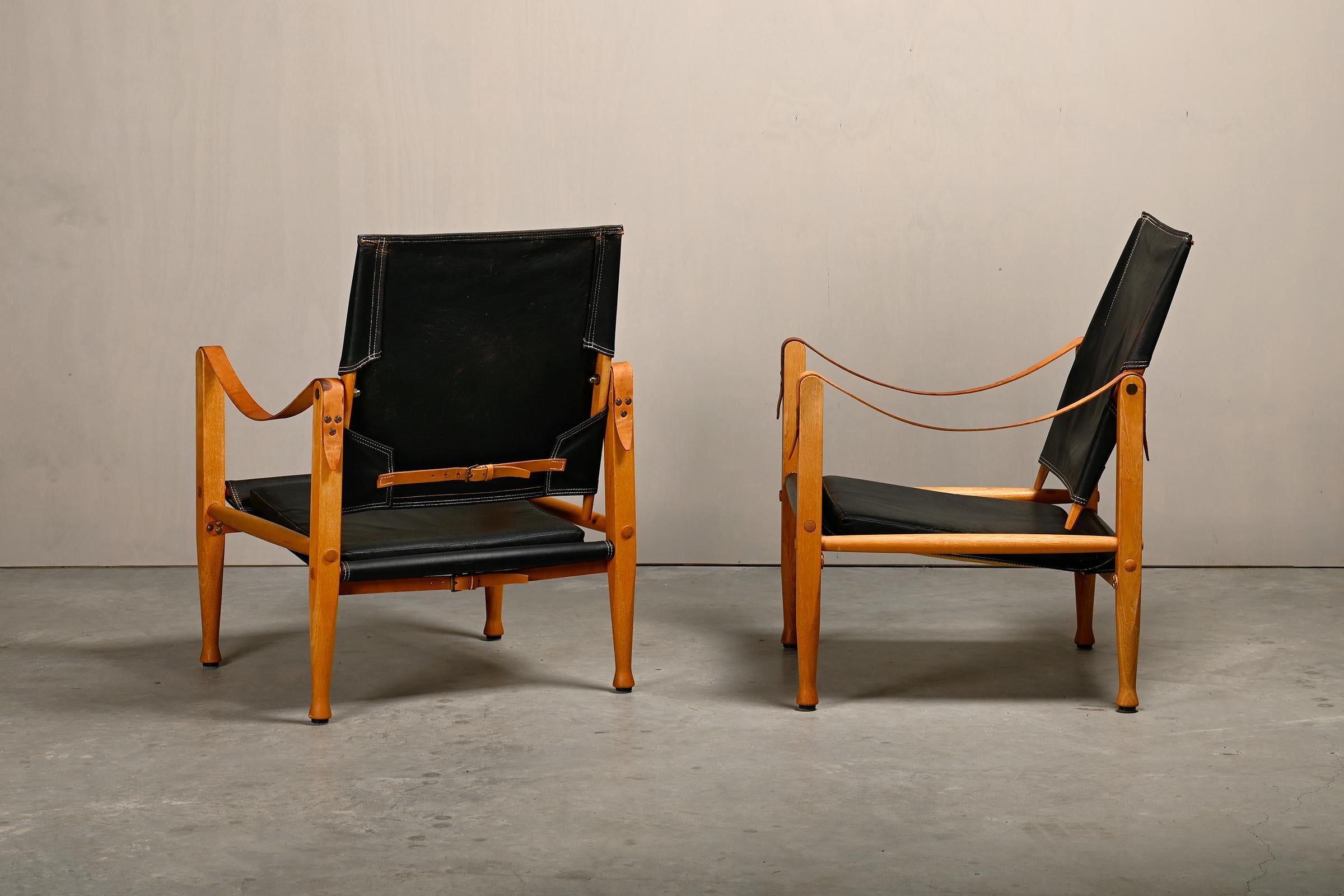 Iconica coppia di poltrone Safari (modello KK 47000) disegnata da Kaare Klint nel 1933 e prodotta da Rud Rasmussen, Danimarca. Struttura in legno di frassino rivestita con seduta, schienale e cuscino in pelle nera. Braccioli e cinghie in pelle pieno