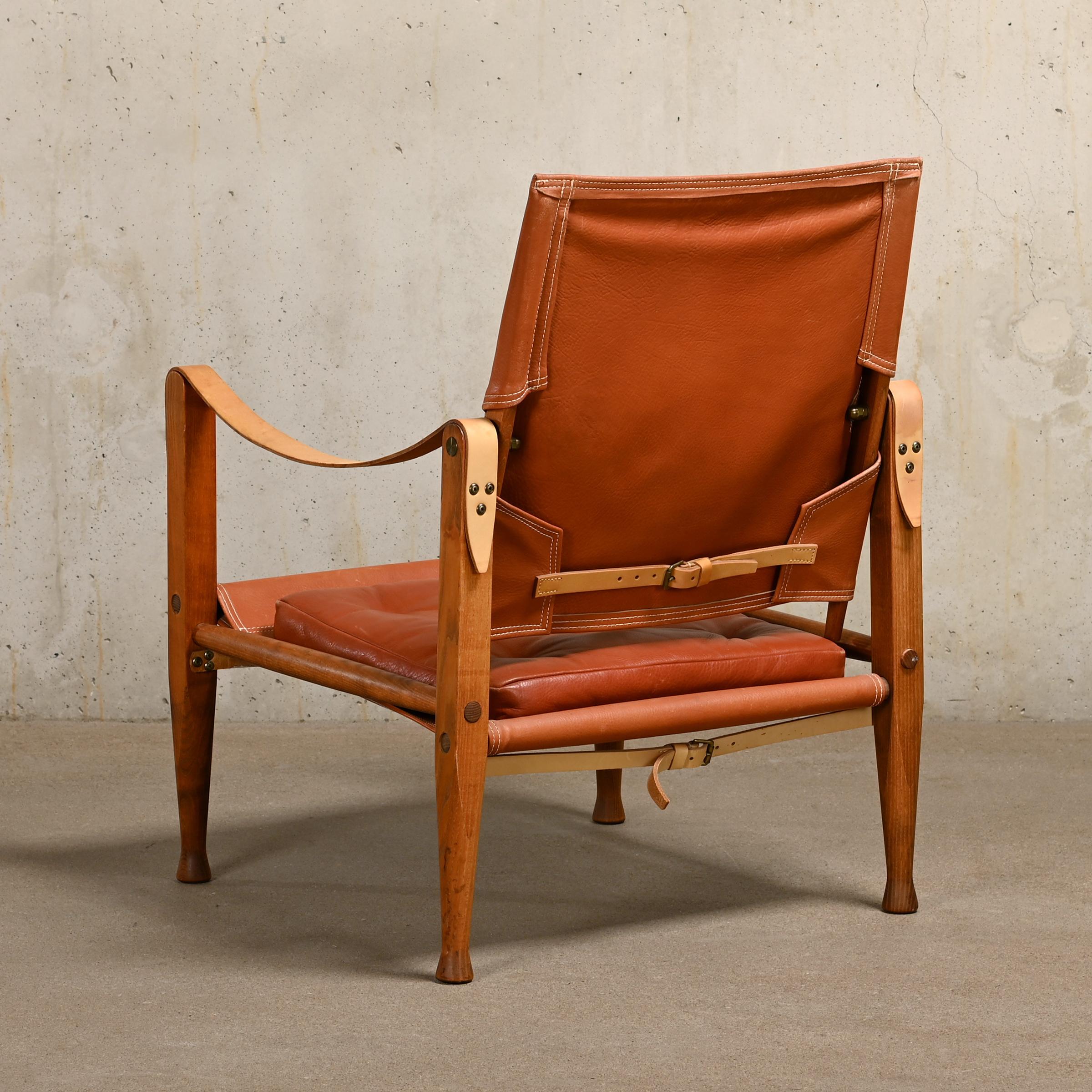 Iconic Safari armchair (model KK 47000) designed by Kaare Klint in 1933 and manufactured by Rud Rasmussen, Denmark. Ash wooden frame upholstered with brown leather seat, back and losse cushion. Armrests and straps with full grain leather. The chair
