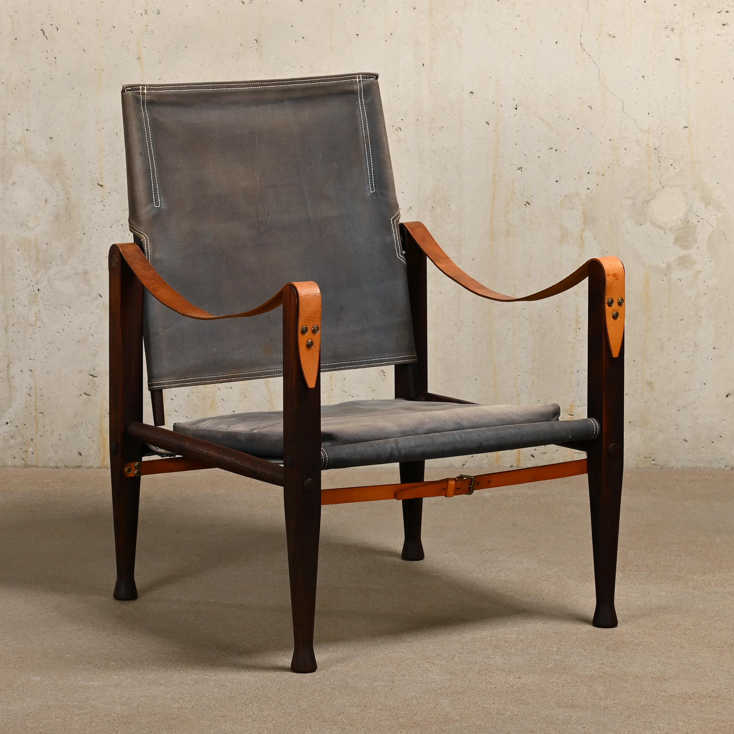 Iconic Safari armchair (model KK 47000) designed by Kaare Klint in 1933 and manufactured by Rud Rasmussen, Denmark. Dark brown stained Ash wooden frame upholstered with grey / blue canvas seat, back and losse cushion. Armrests and straps with full