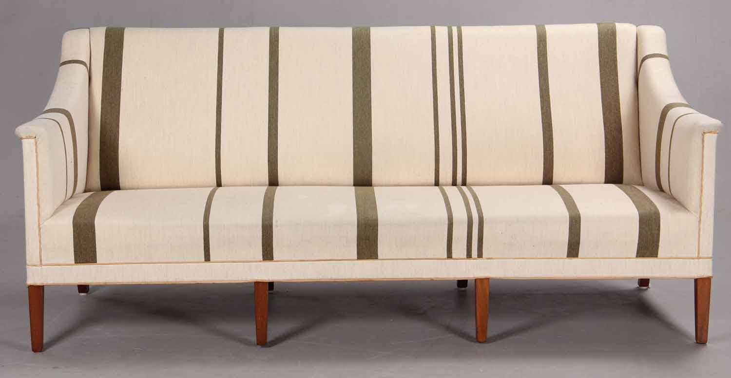 Three-seater sofa with eight tapering mahogany legs. Sides, seat and back upholstered with striped savak wool presumably in the last 10-20 years with natural leather pipings. Model 6092. Designed 1940. Made by Rud. Rasmussen Cabinetmakers.